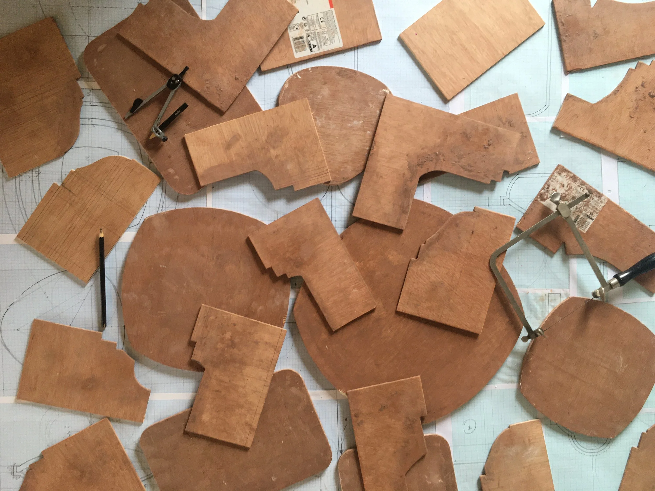 Multiple irregularly shaped wooden tiles placed on a grid-patterned surface with technical drawings and compasses.