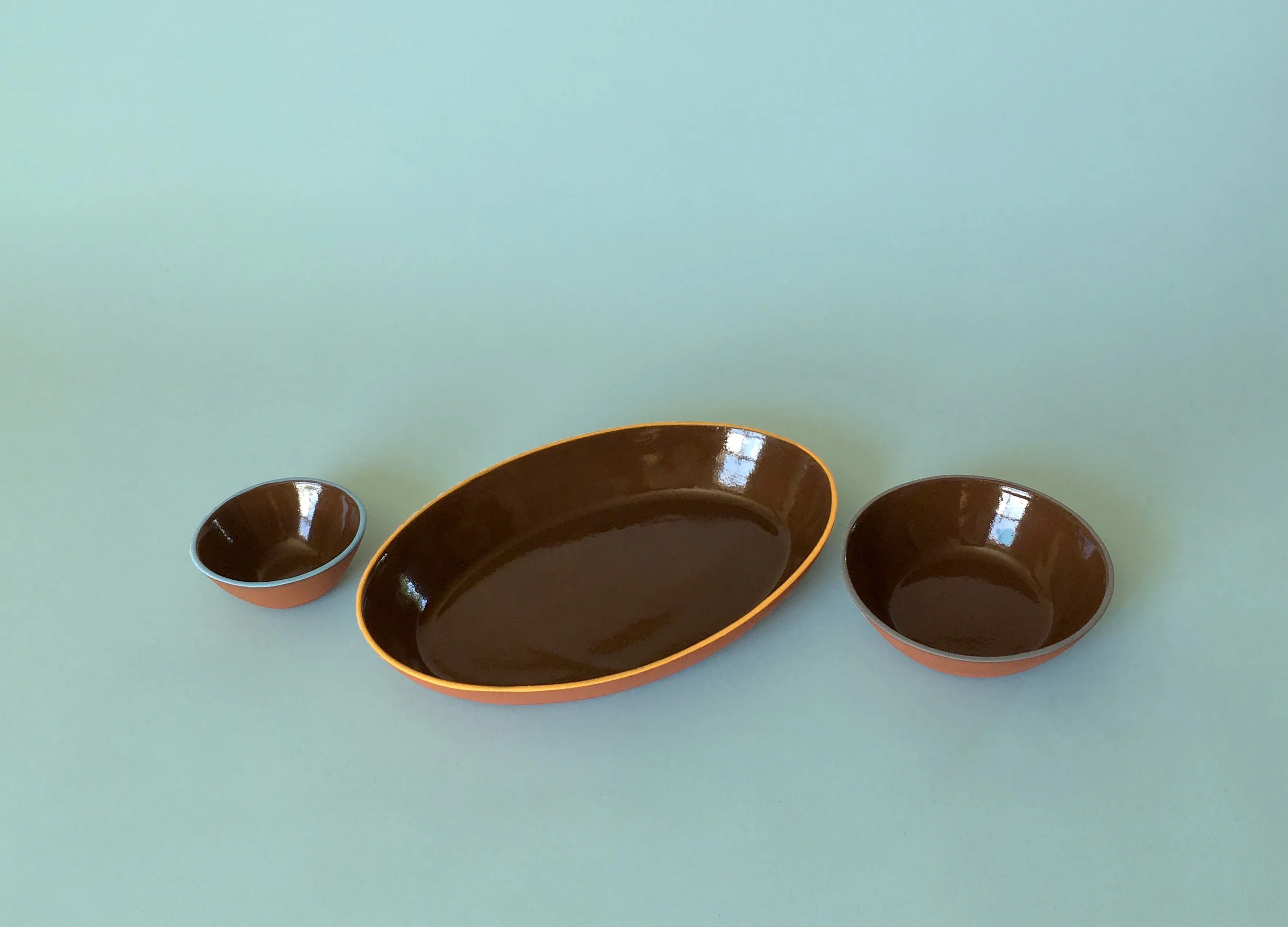 Three ceramic bowls on a light green surface, with larger oval and two smaller round bowls.