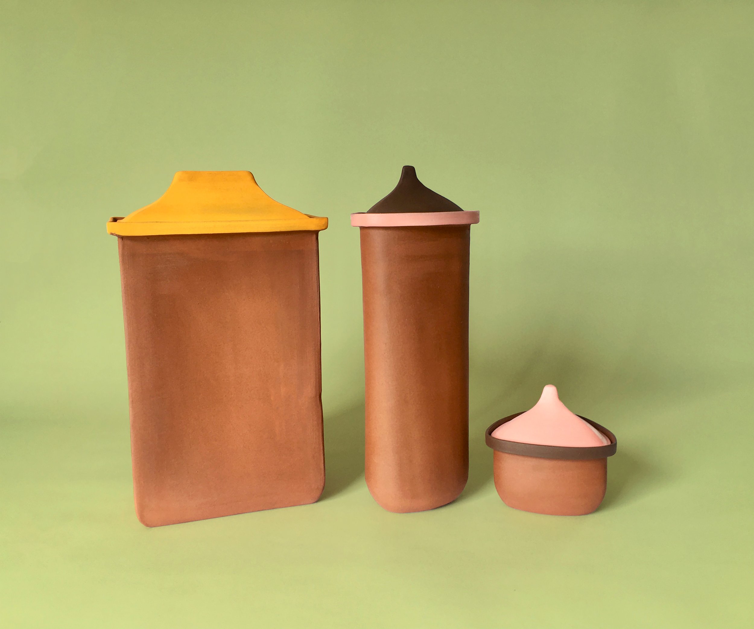 Three ceramic containers with lids, two tall cylinders and one small bowl, placed on a light green background.