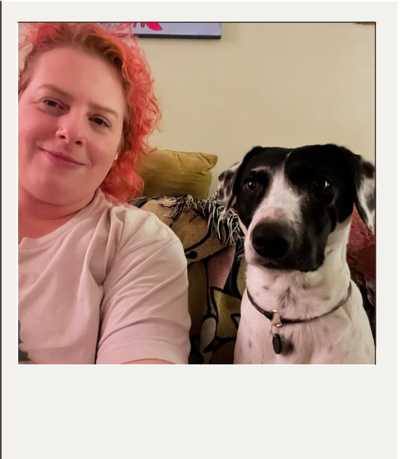 A woman with curly red hair smiling next to a black and white dog on a couch.
