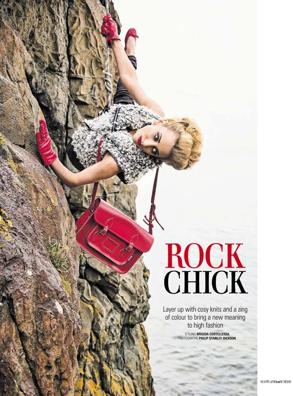 Fashion Editorial Magazine with Elaine Ford climbing and scaling up a seacliff with red bag and gloves. Outdoor fashion model