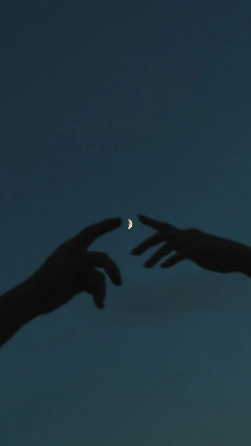 Two silhouetted hands reaching toward a crescent moon in a dark sky.