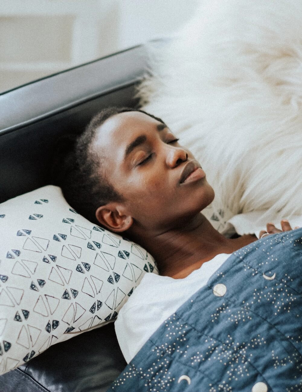 Person sleeping peacefully on a bed with patterned pillow and a quilted blanket.