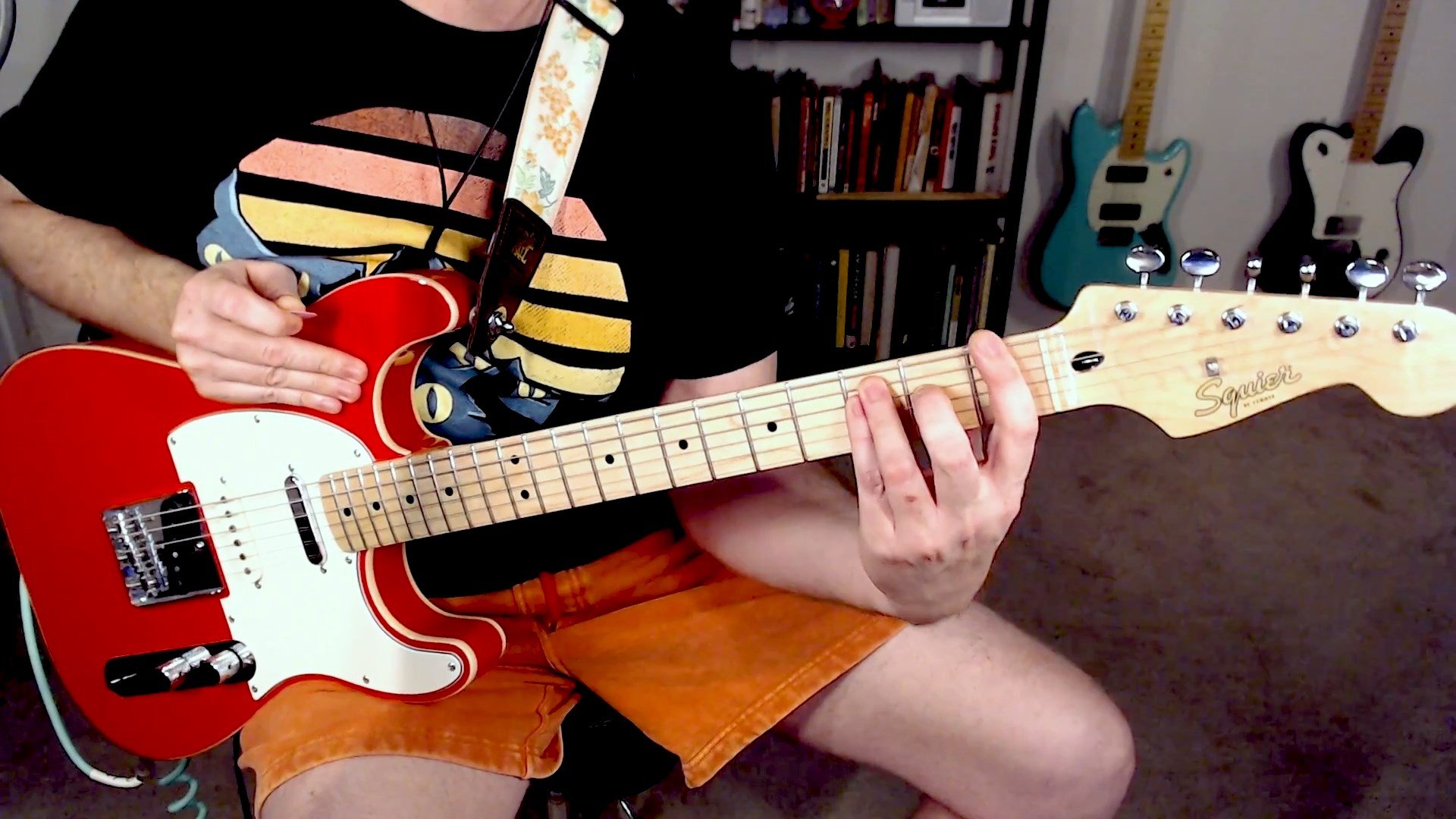 A crystal clear image of a Fiesta Red Squier Nashville Telecaster, held by a person wearing a cat shirt, Chubbies orange shorts, while he displays how to fret a F Major chord