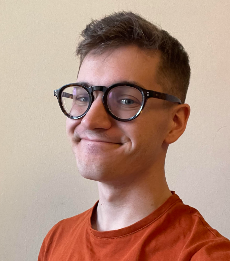 A young man with short brown hair and glasses, smiling in front of a beige wall.