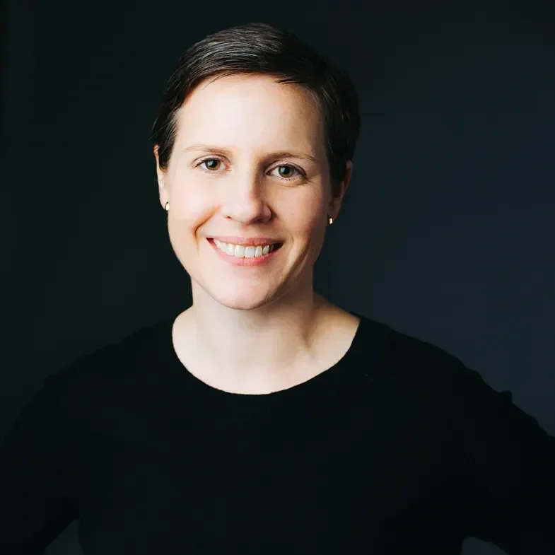Portrait of a woman with short dark hair, wearing a black top, smiling against a dark background.