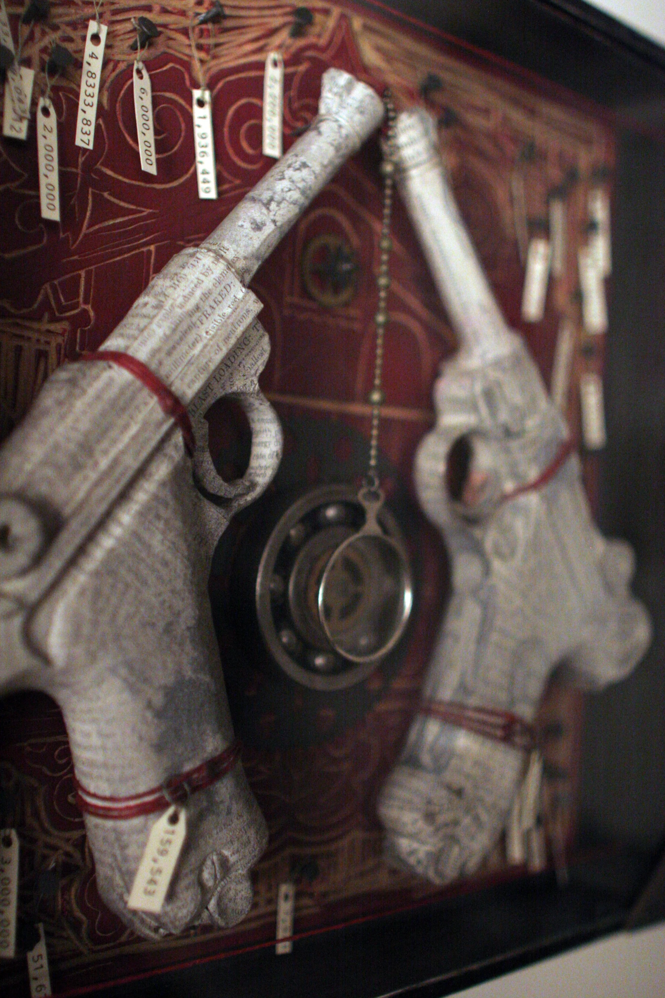 Two antique pistols made of newspaper, displayed with various tags and a clock in the background, inside a display case.