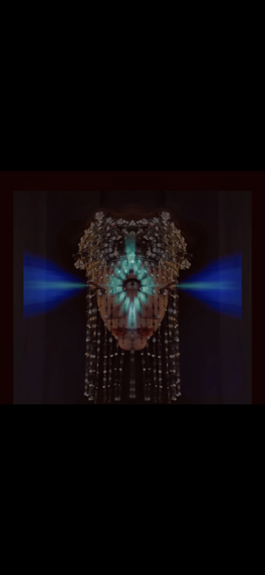 A mirror image of a woman with a bouffant hairstyle, wearing a beaded dress, illuminated by blue light beams from the sides.