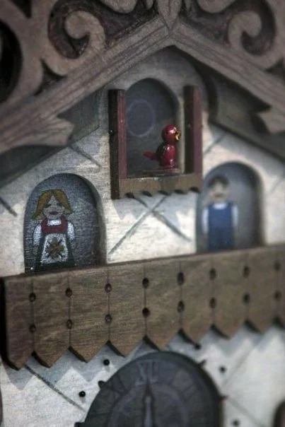 Close-up of a decorative wooden cuckoo clock with painted figures of a girl, a boy, and a small bird inside the clock box.