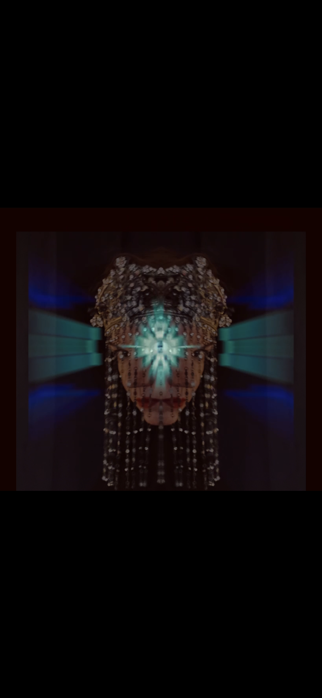 Abstract digital artwork with symmetrical, kaleidoscopic patterns in shades of blue, teal, and brown, forming a central glowing figure resembling a stylized face or mask.