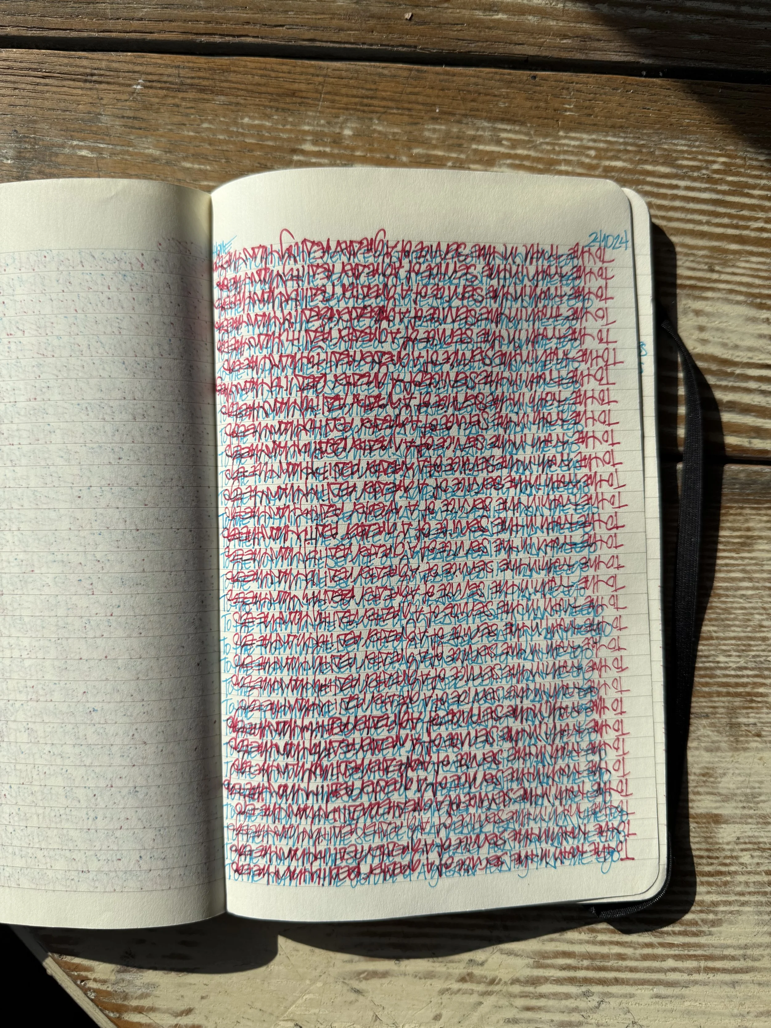 A notebook opened to pages filled with colorful overlapping handwriting in red, blue, and black ink, on a wooden surface.