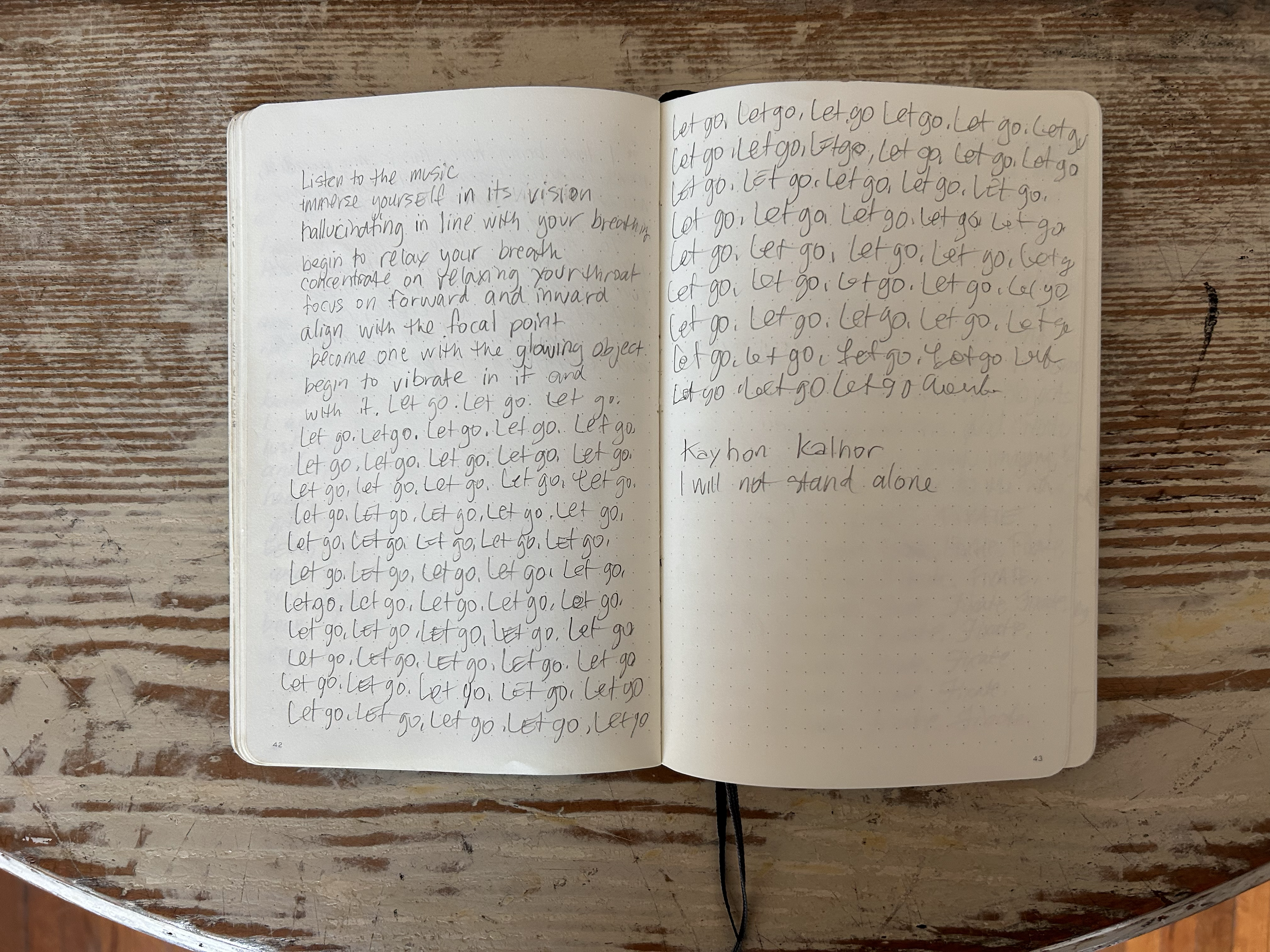 An open notebook on a wooden surface with handwritten notes. The left page contains a paragraph with instructions about music and relaxation, while the right page has repeated handwriting of the phrase 'Let go' and the words 'Kayhan Kalhor' and 'Will