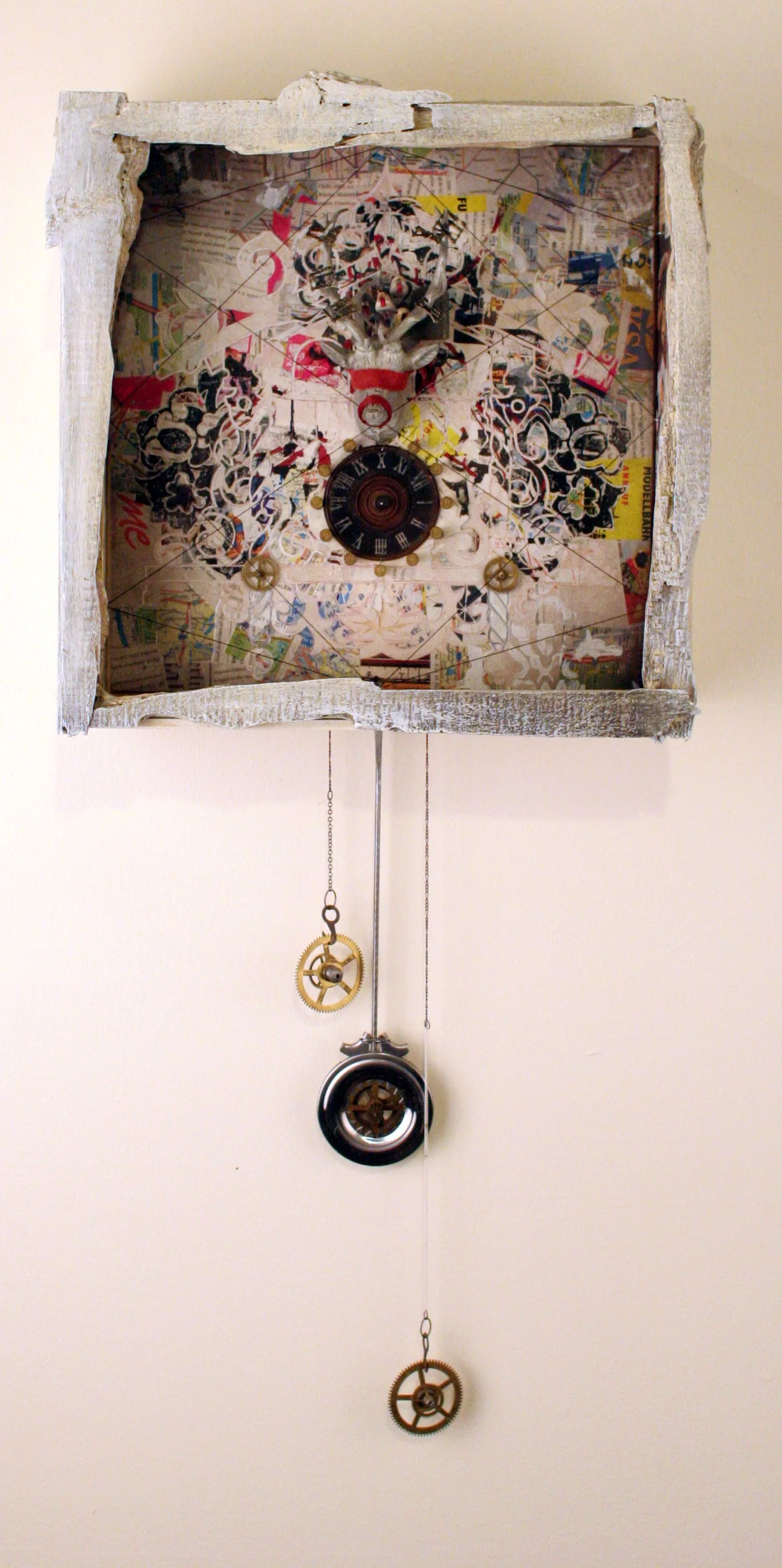 A mixed media wall clock with a distressed white wooden frame, decorated with collage elements and mechanical gears hanging below.