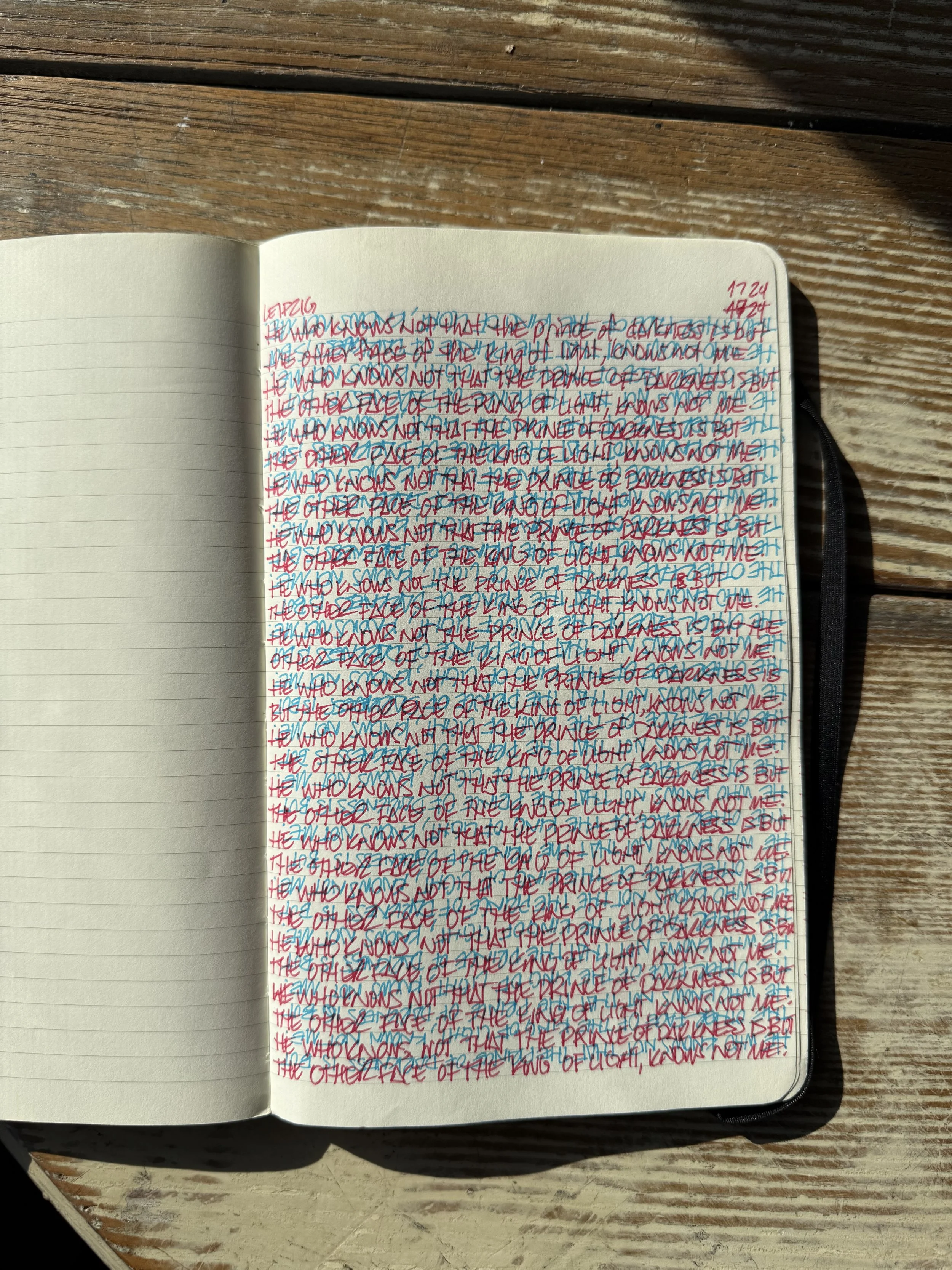 Open notebook on a wooden surface with handwritten notes in red and blue ink, overlapping lines.