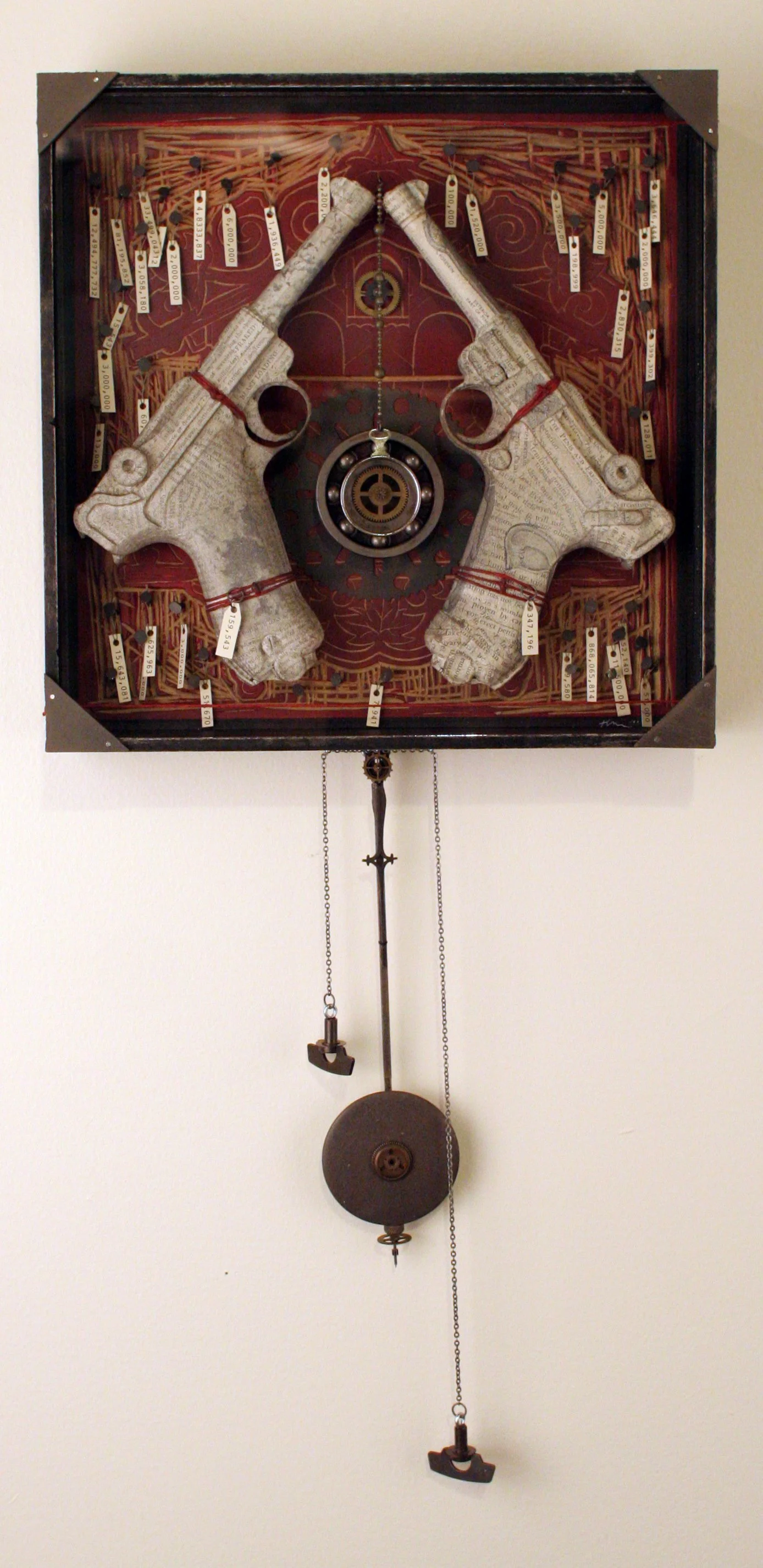 A wall-mounted clock with a decorative frame featuring two revolver-shaped objects, a chainsaw, and a circular pulley with chains hanging down.