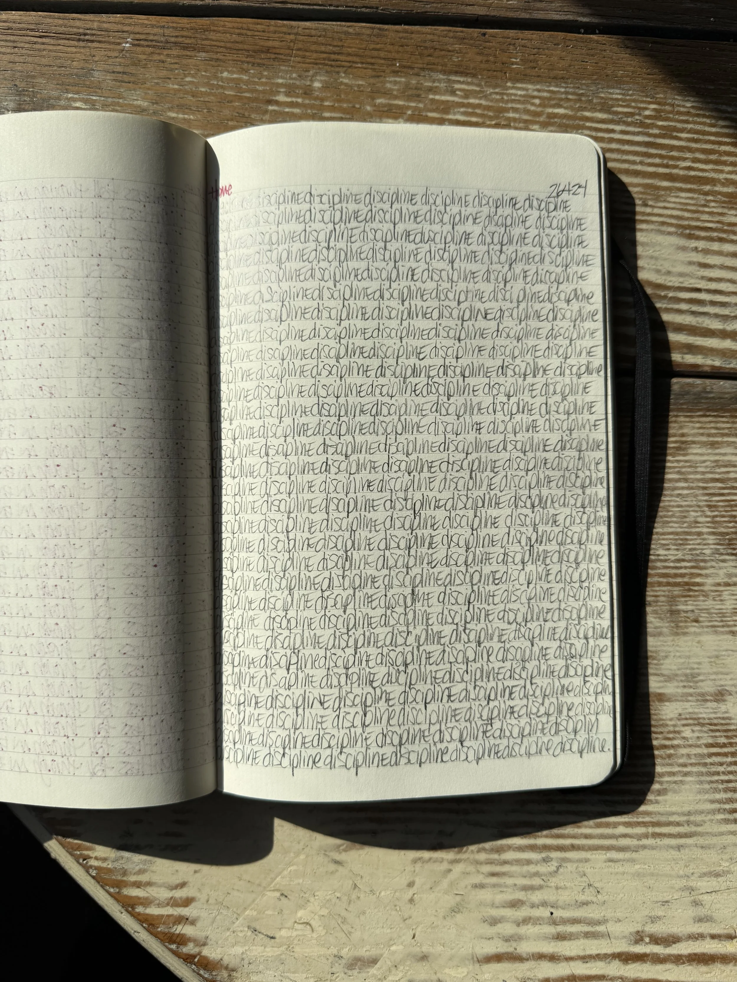 Open notebook with handwritten text on a wooden surface, sunlight casting shadows.