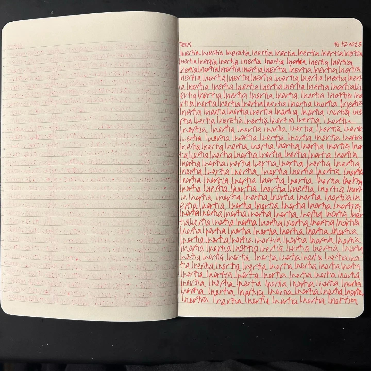 Open notebook with one page filled with red handwritten words 'Inertia' repeated multiple times and the other page blank with faint red lines. The date 16-17-2023 is written in red on the top right corner.