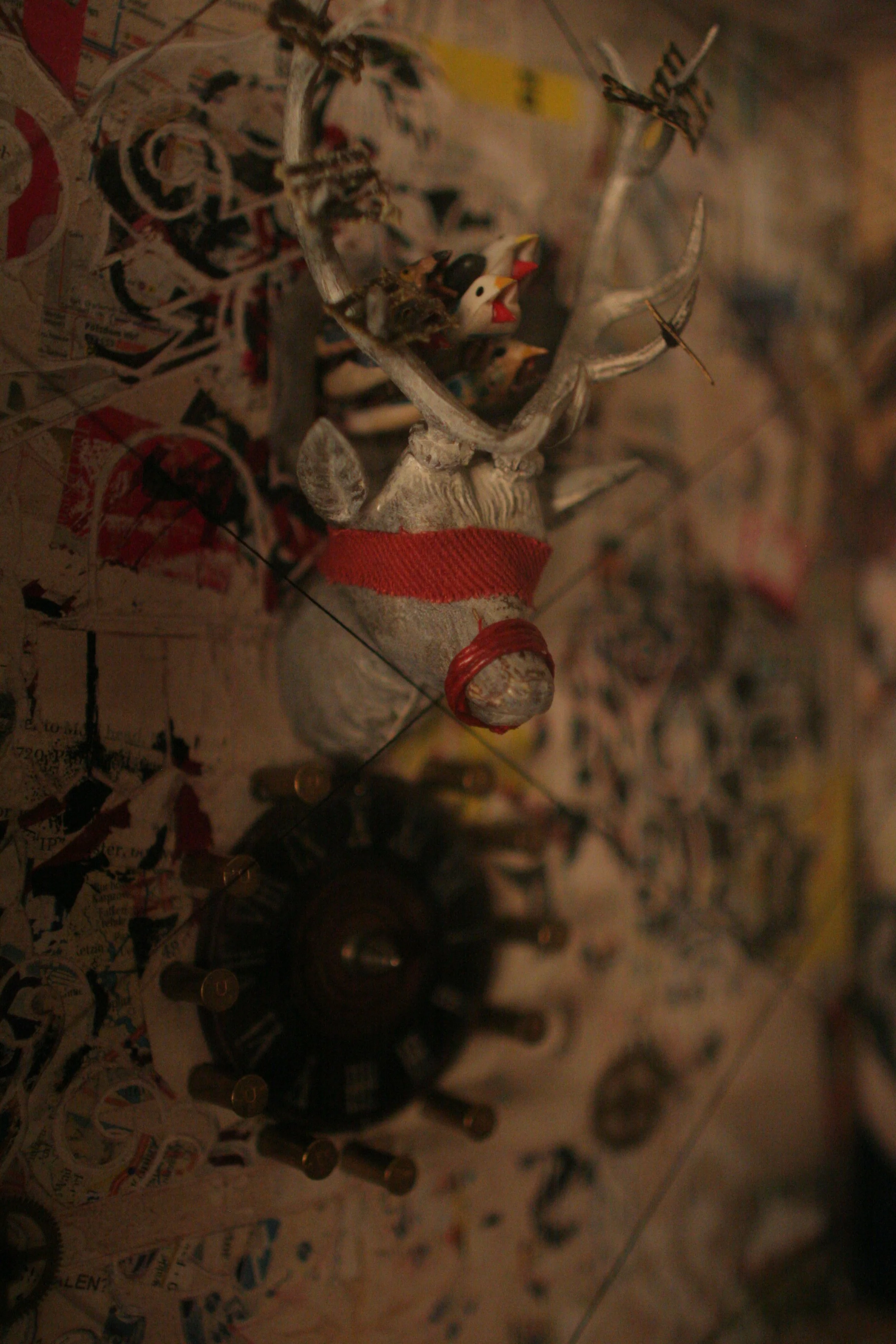 Toy reindeer with a red ribbon around its neck, surrounded by various small figurines, a circular object resembling a vintage safe dial, and scattered torn paper.