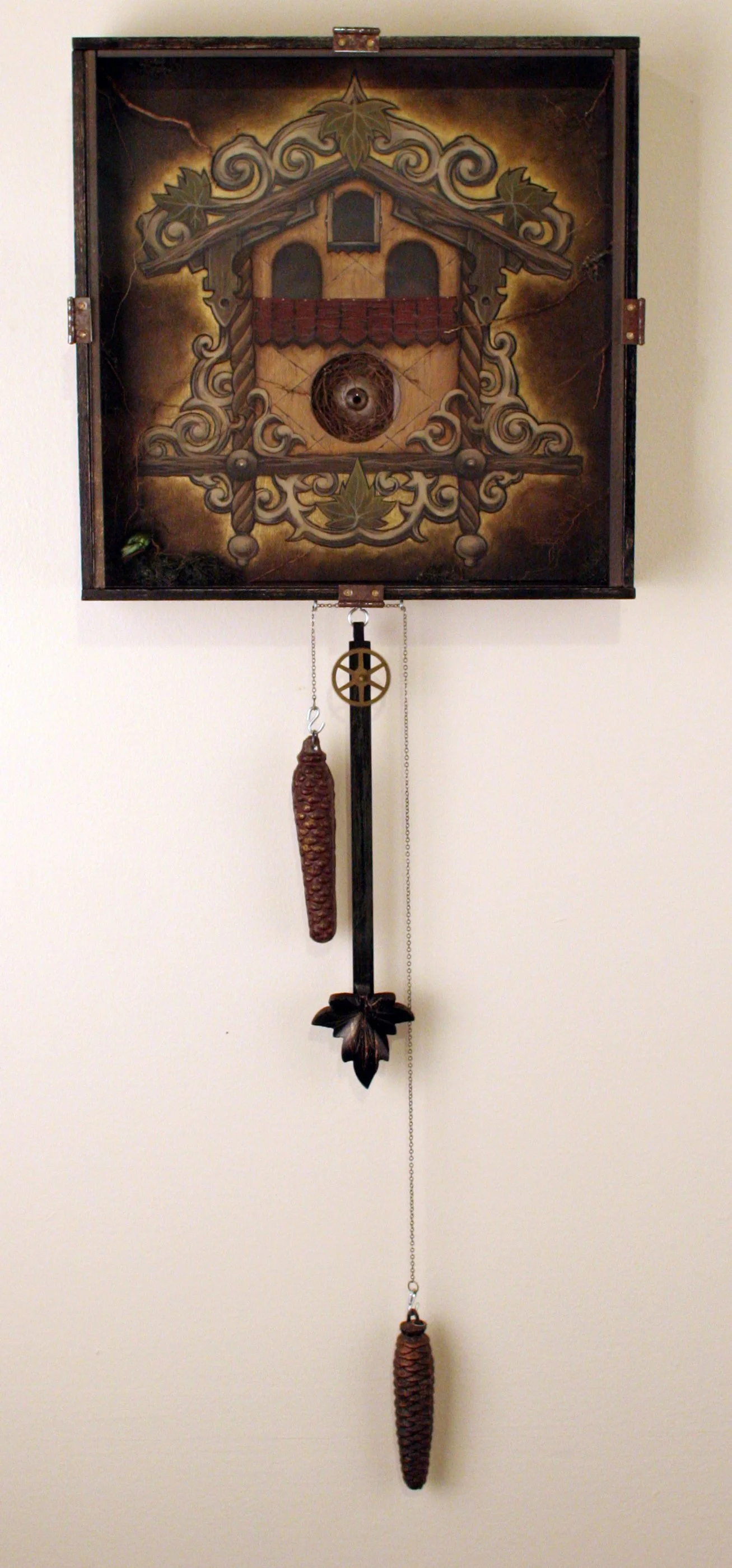 A decorative cuckoo clock with a house design, featuring pine cones hanging as weights, set against a plain wall.