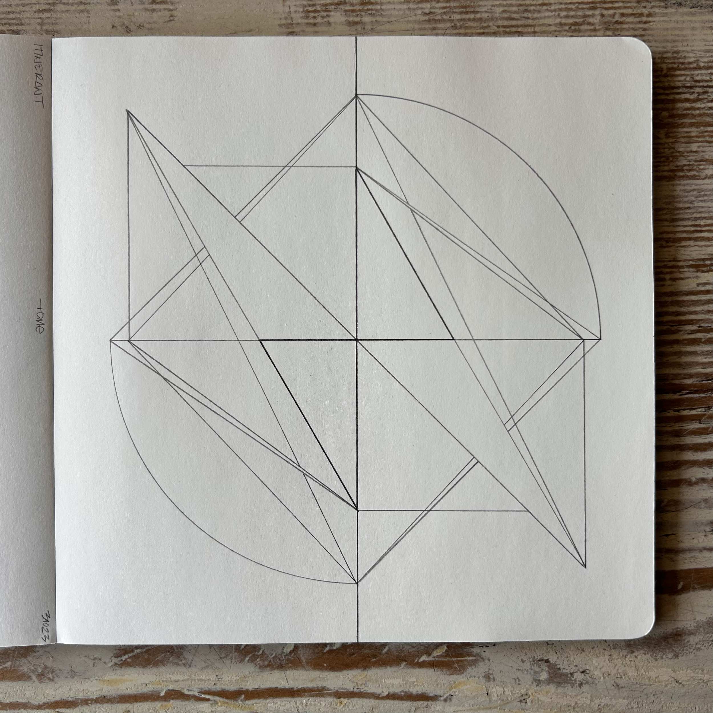 Sketch of geometric shapes with lines and circles drawn in a notebook on a wooden surface.