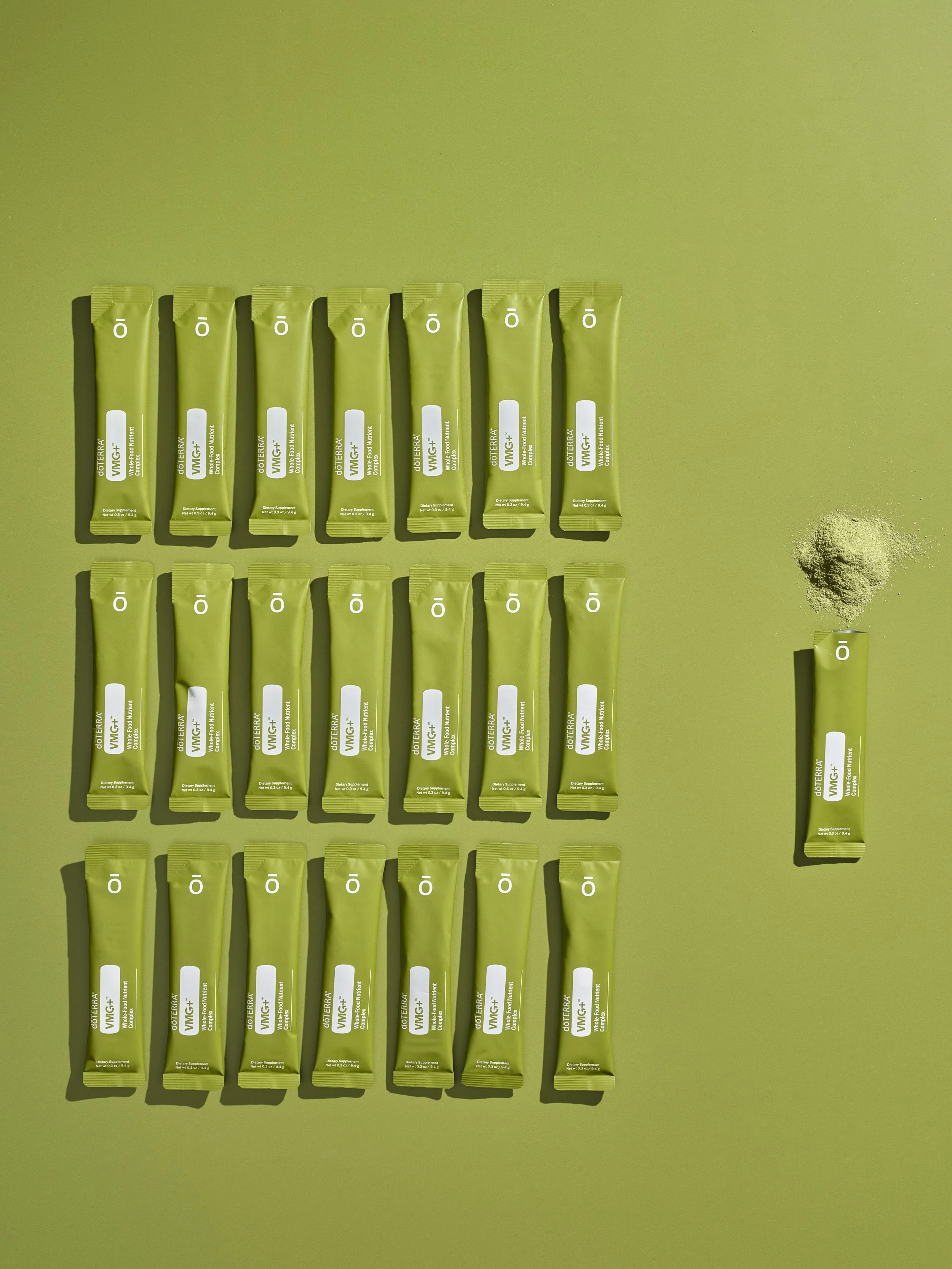 Multiple packets of doTERRA Mito2Max dietary supplement arranged on a green surface with a single packet and a pile of powder to the right.