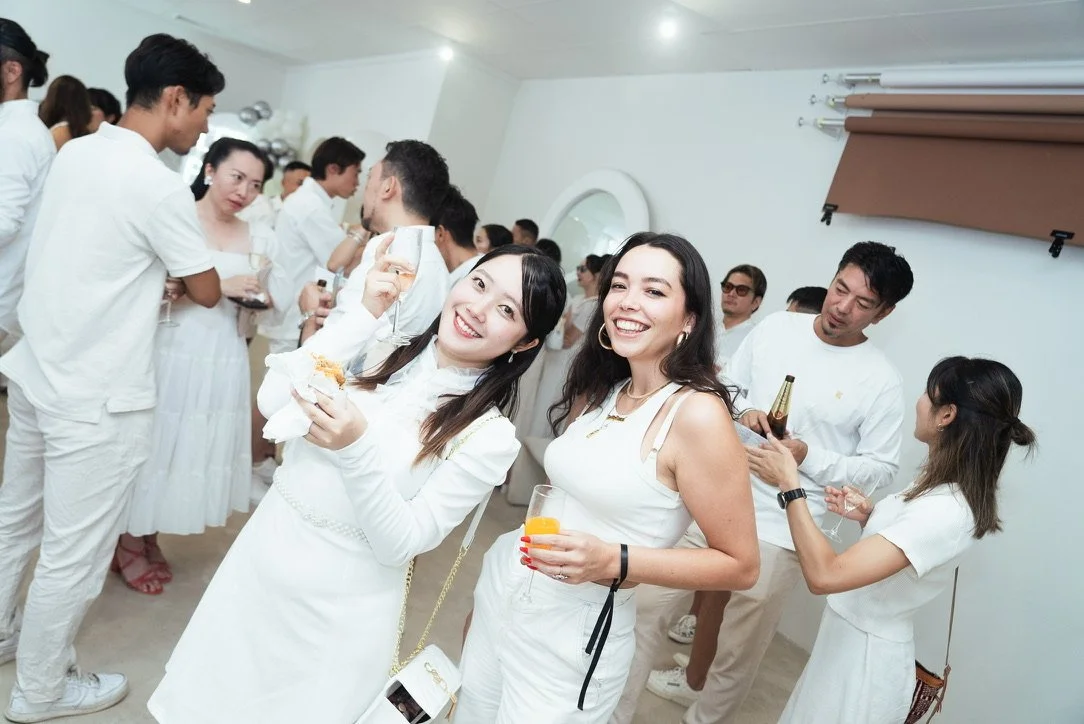 People at a social gathering or party, mostly dressed in white, smiling, holding drinks, and enjoying themselves