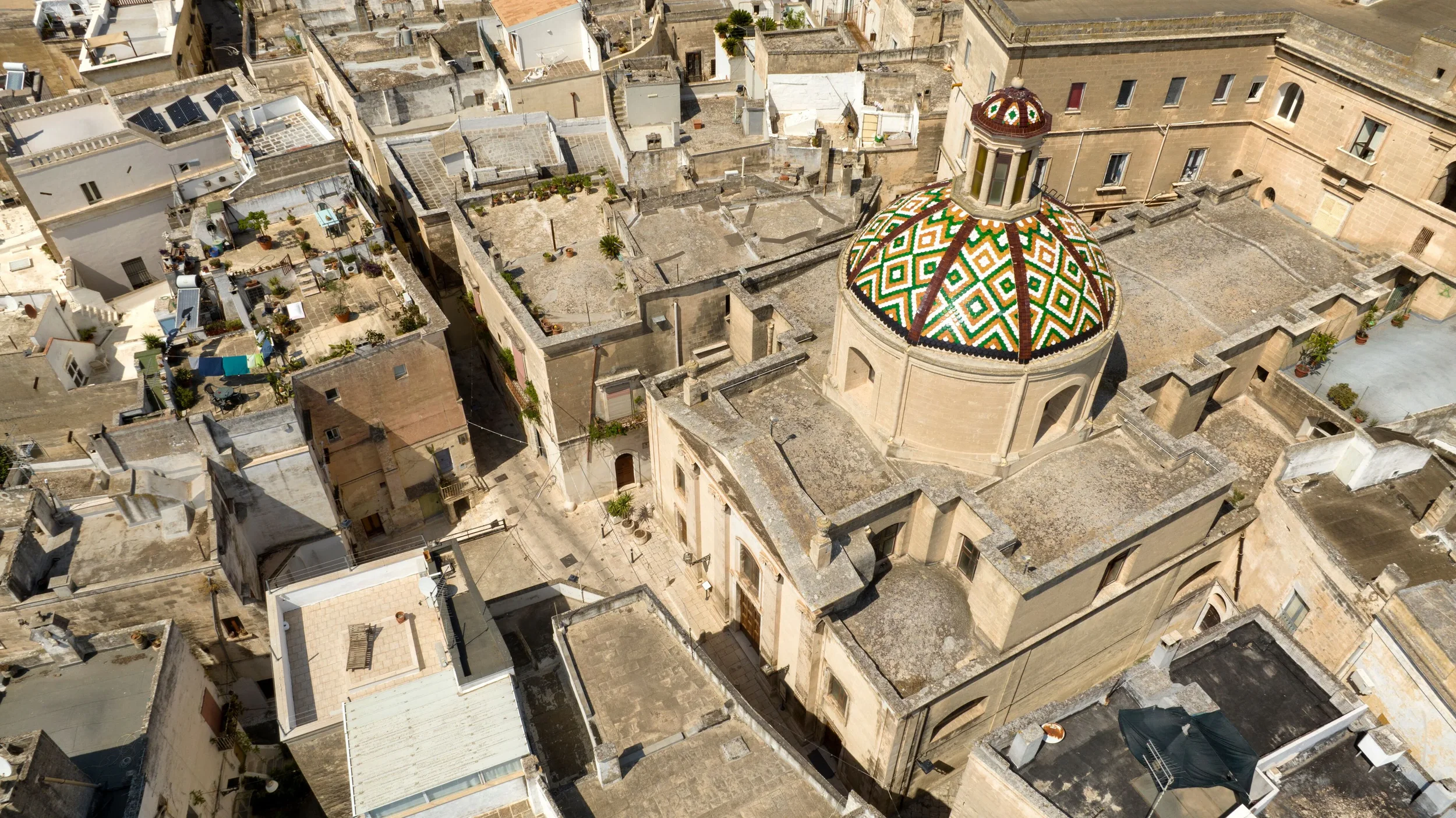 Historical stone church with round clock and dome, surrounded by colorful flowers and a courtyard.