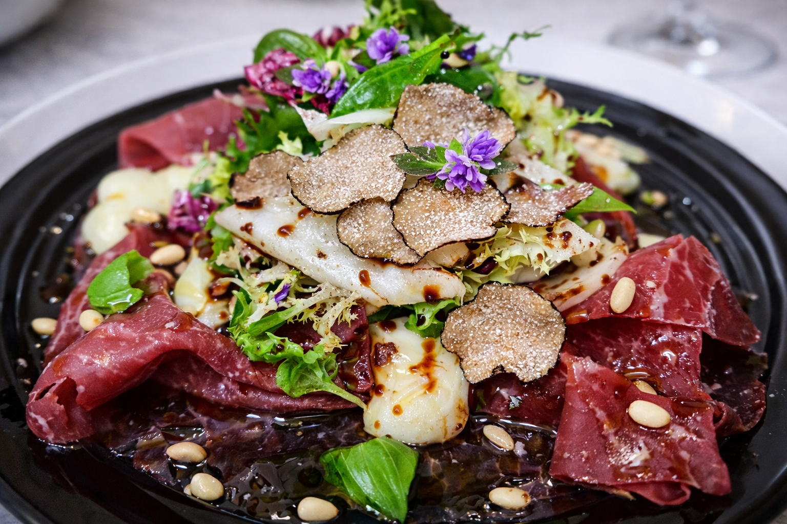 Bresaola madurada con trufa negra laminada, reducción balsámica y flores frescas, plato gourmet creado por un chef profesional en el Algarve, Portugal.