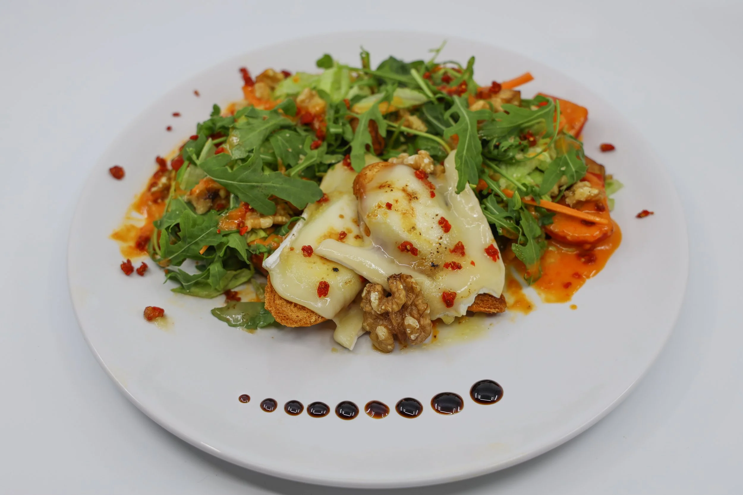 Ensalada de rúcula con queso chèvre gratinado, nueces y salsa artesanal, creada por un chef profesional en el Algarve.