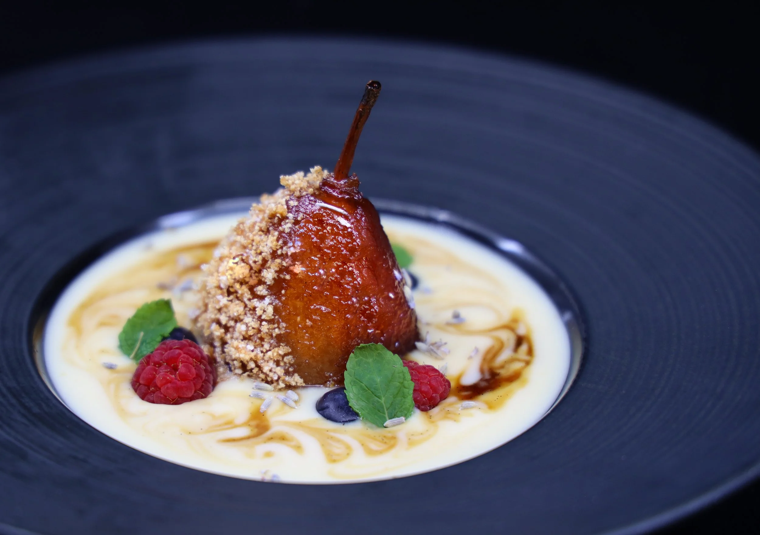 Delicado postre con pera caramelizada sobre crema ligera de vainilla, frutos rojos y un toque gourmet, creación de un chef en Portugal.