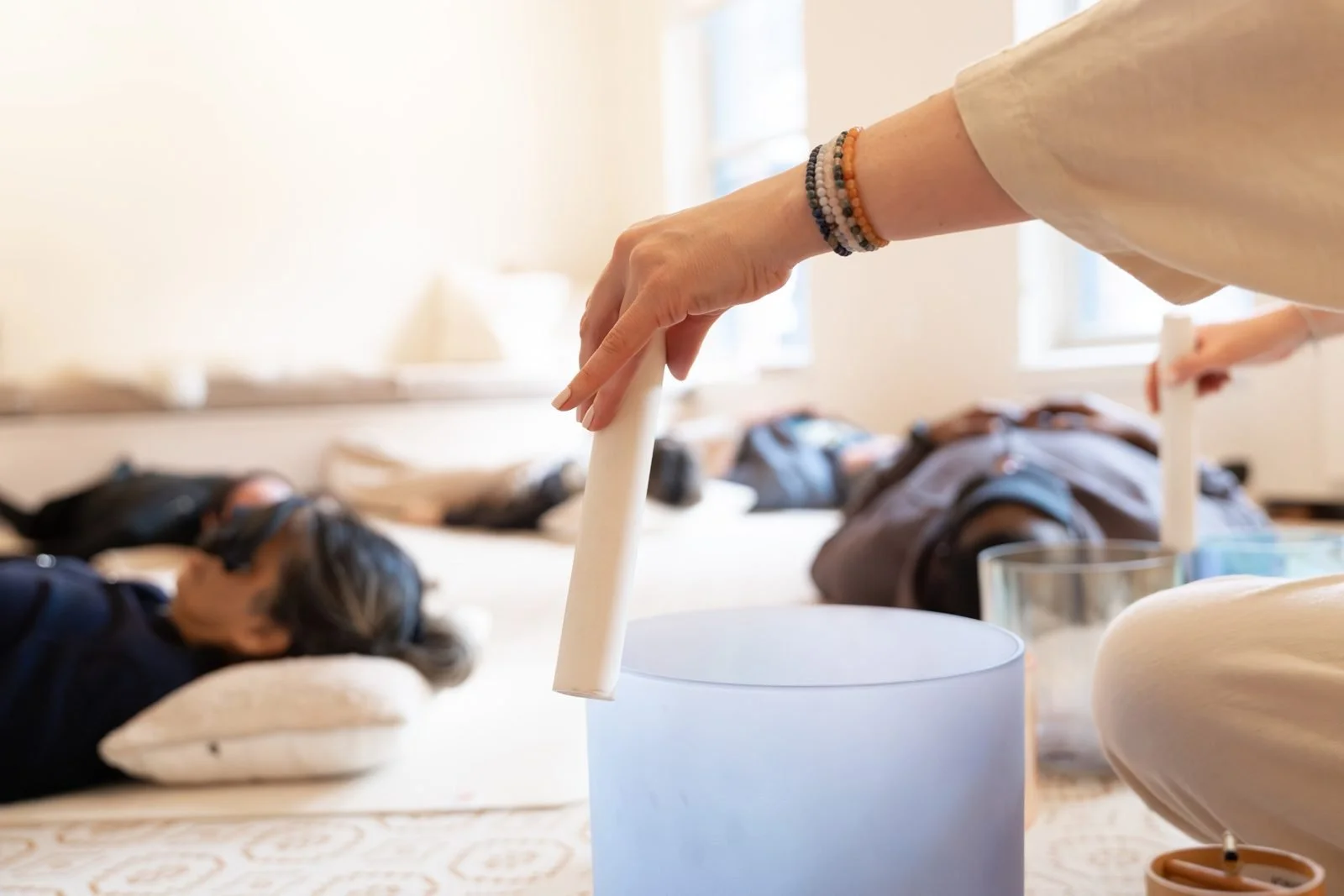 Katie Boysen playing a crystal singing bowl beside a client resting on a pillow during a private sound bath