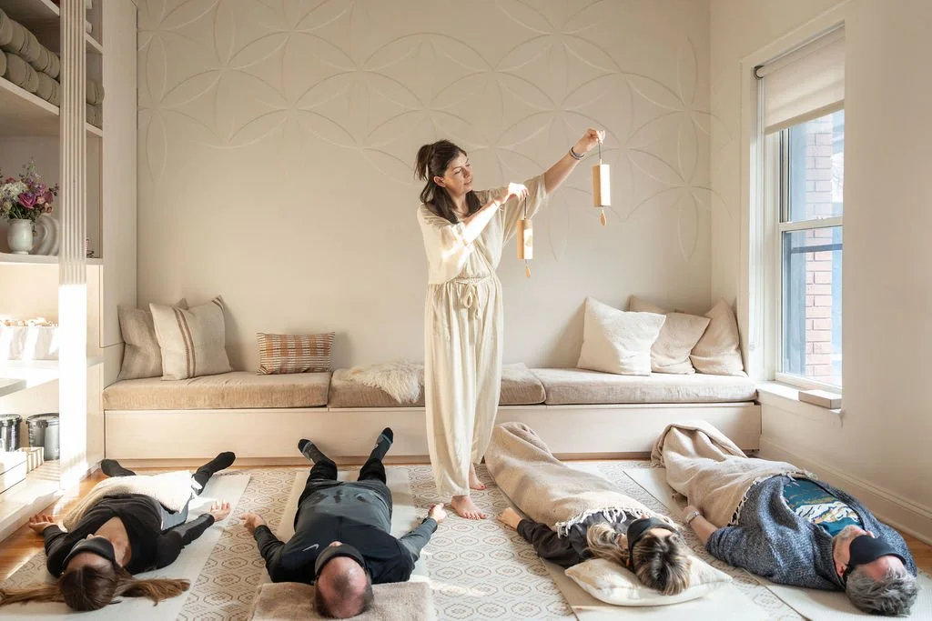Katie Boysen leading a sound session in a cozy, well-lit room with four people lying on the floor on mats and blankets.