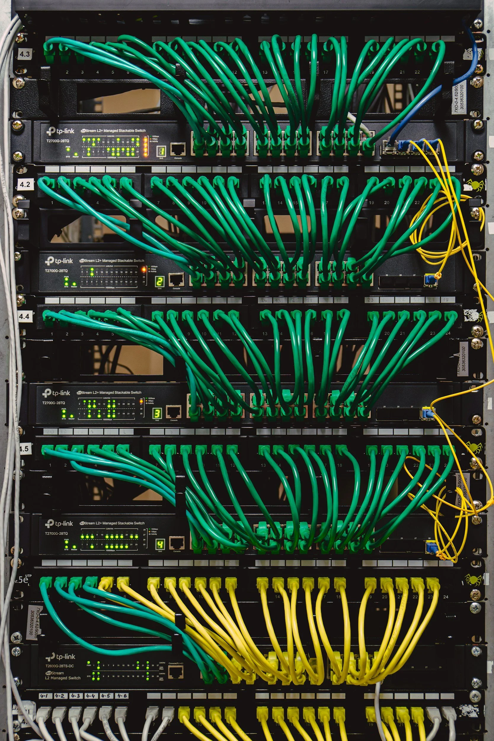 A server rack containing multiple network switches with green and yellow Ethernet cables connected to them.