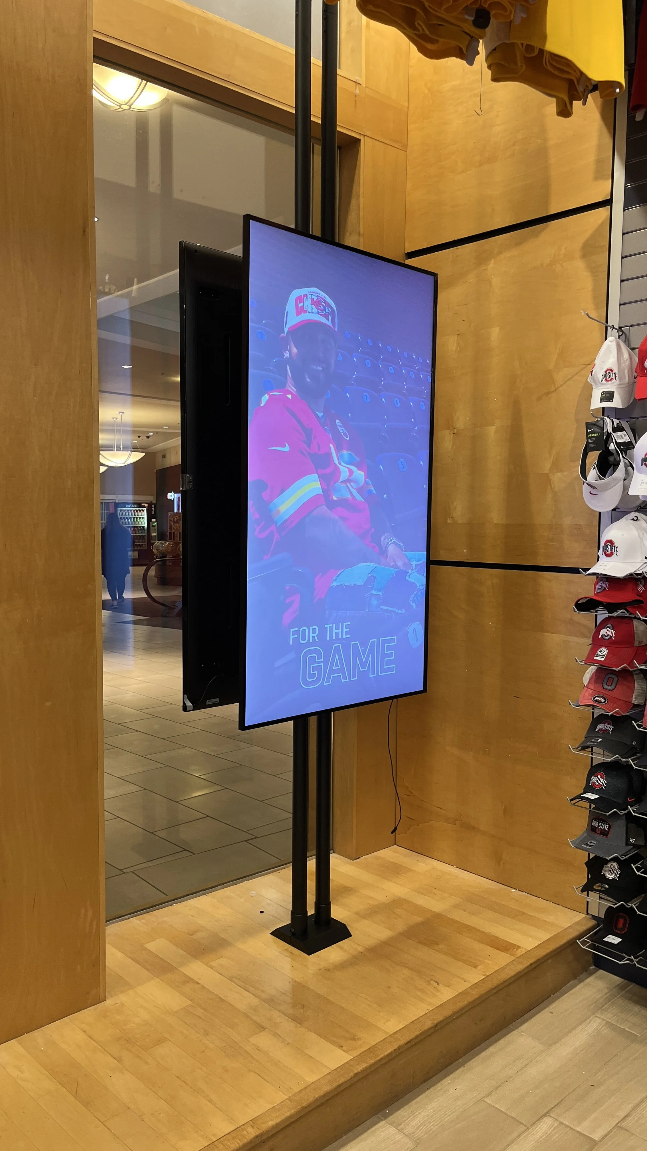 Digital display screen in a store showing a person in a football jersey with the text "For the Game" at the bottom.