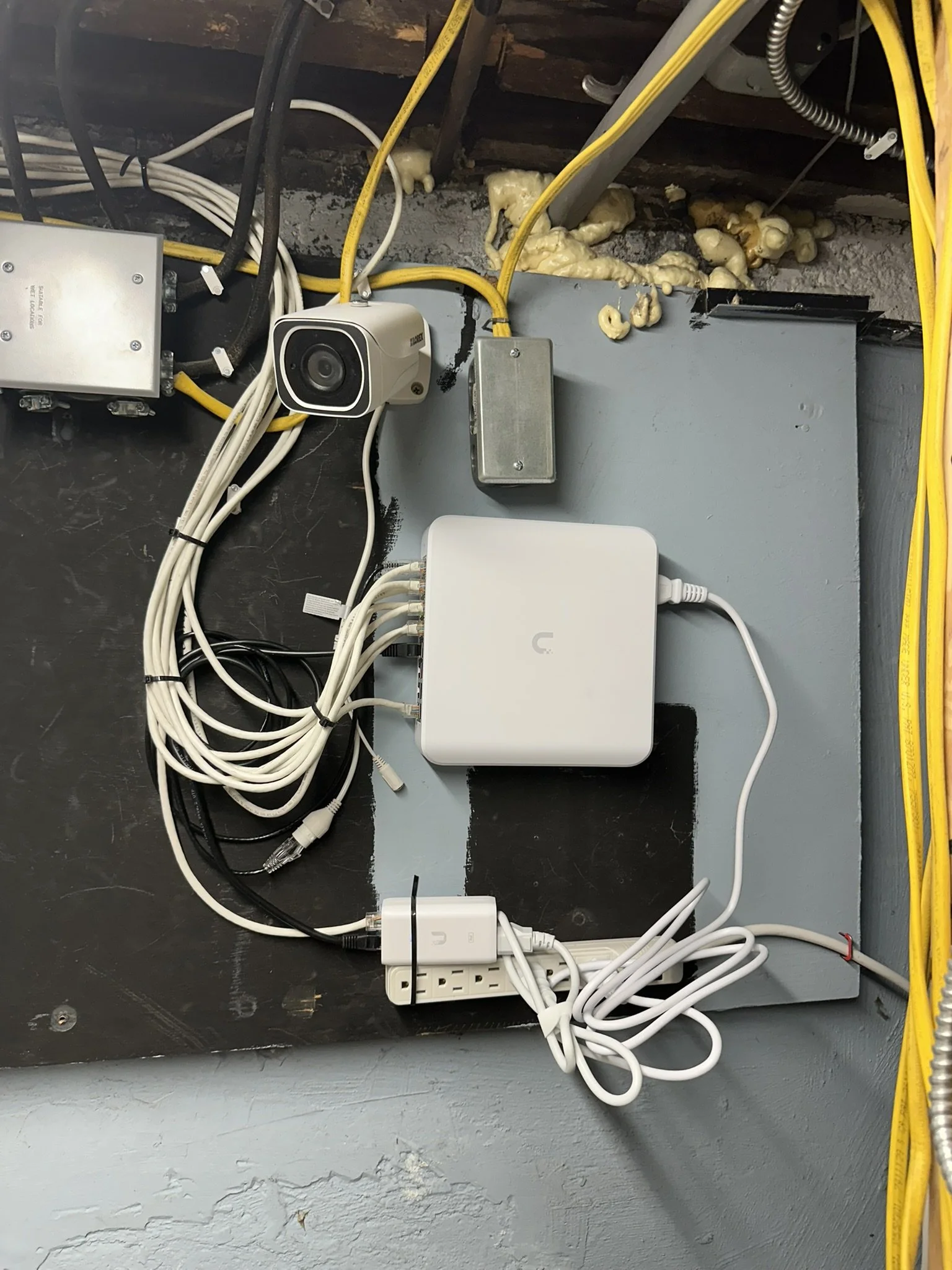 Network equipment and cables mounted on a wall, with insulation and foam around the ceiling.