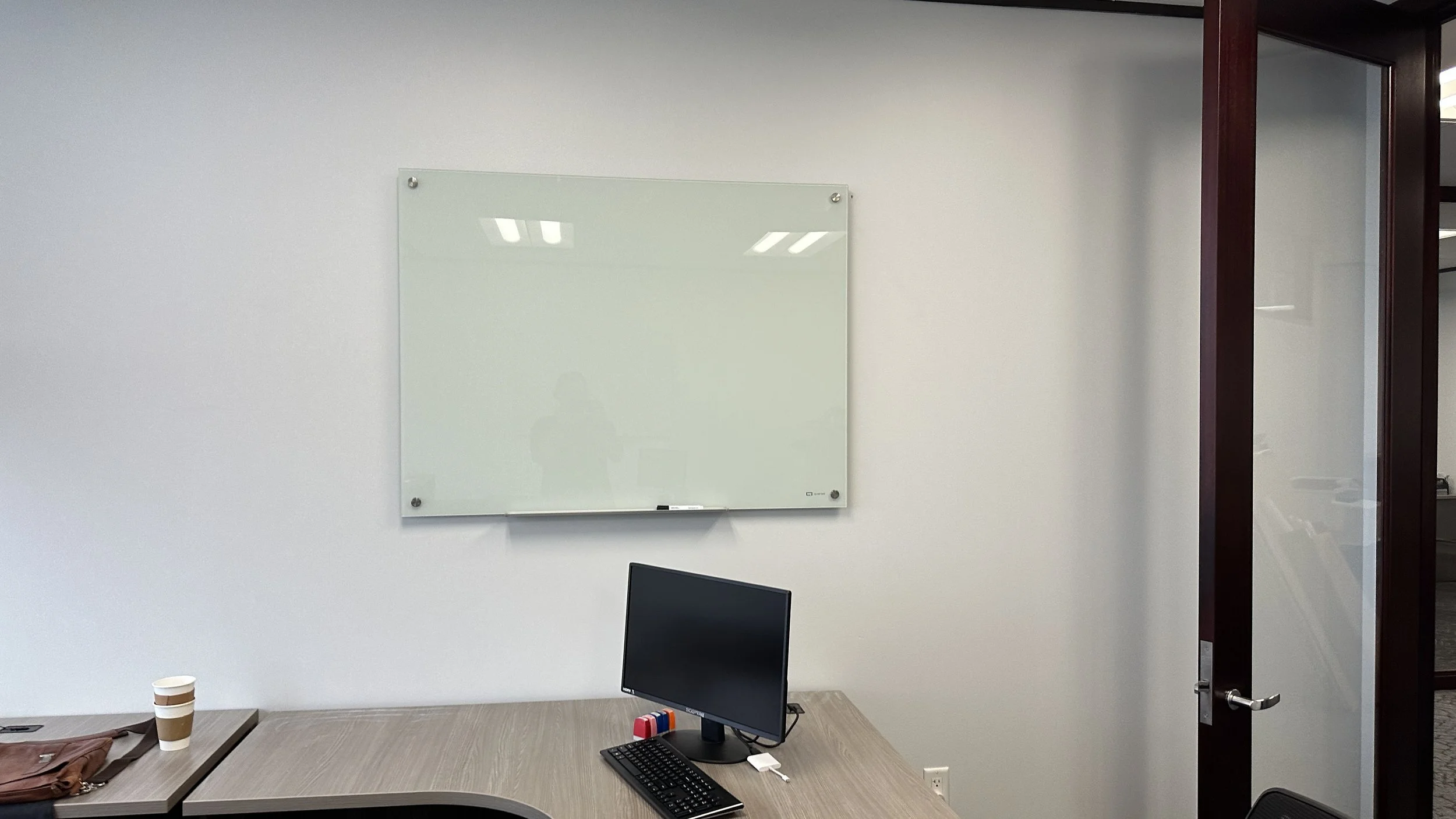 Empty office meeting room with a whiteboard on the wall, a computer monitor on the desk, a keyboard, and a coffee cup.