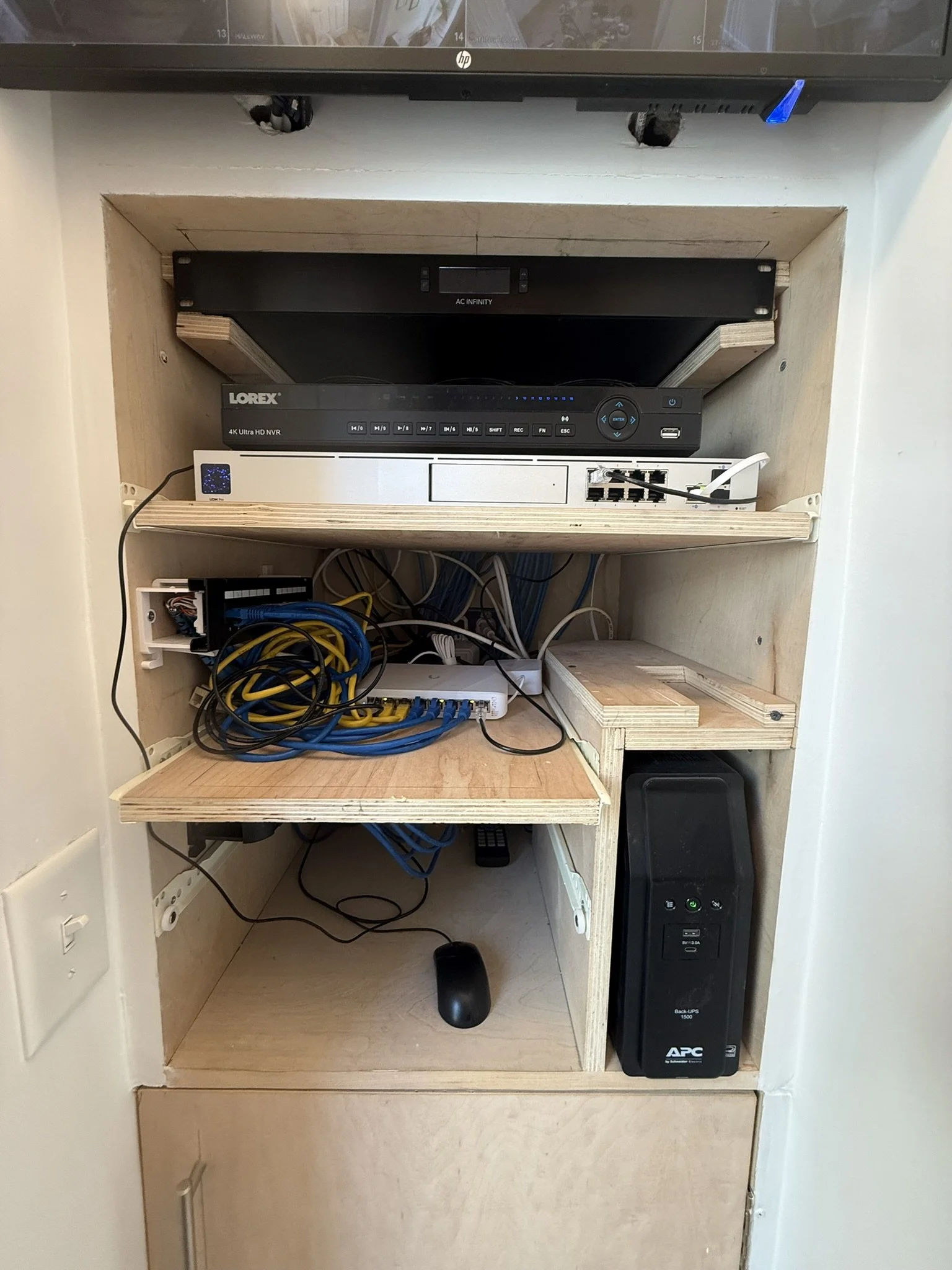 A wooden cabinet housing networking equipment, an unassembled shelf, and an APC backup power supply. On top, an HDTV is partially visible.