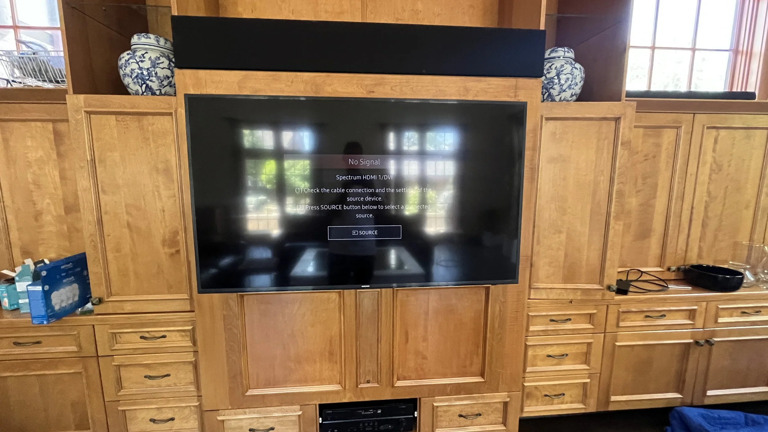 Living room entertainment center with a large flat-screen TV displaying a no signal message, surrounded by wood cabinetry and decorative vases on top.