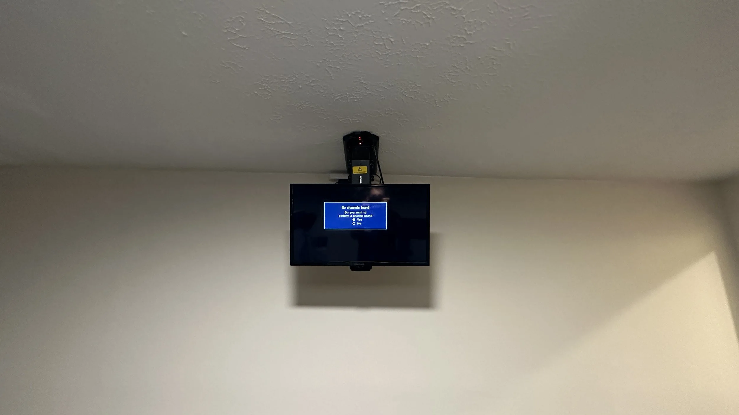 A television mounted on a wall displays a blue screen with a message indicating no channels found and prompting for a channel scan.