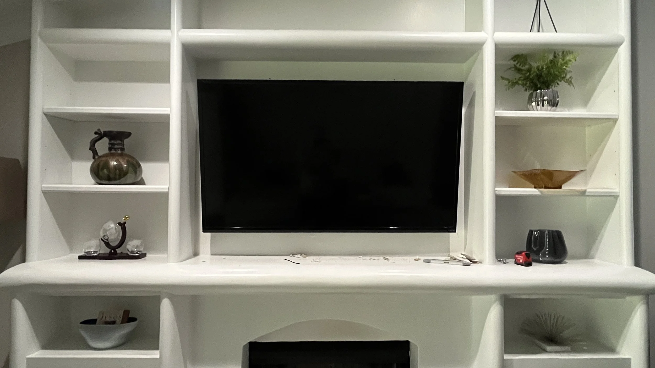 White entertainment center with a black flat-screen TV in the center, decorated with vases, bowls, a small plant, and various decorative objects on the shelves.
