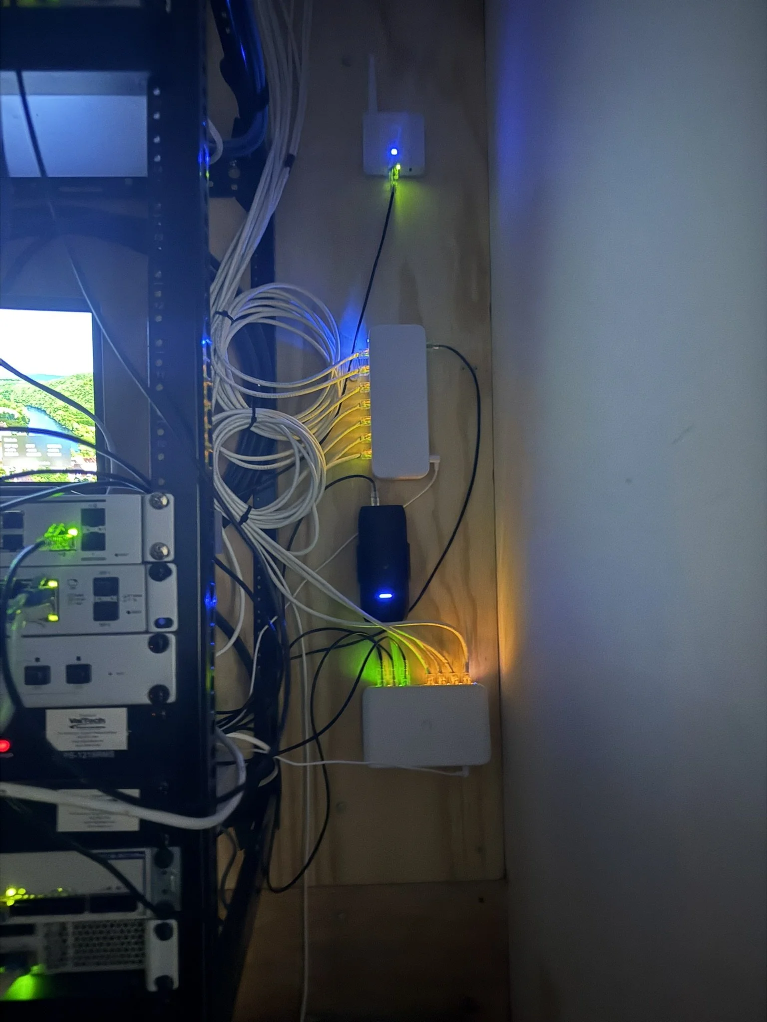A network server rack with cables and electronic devices on a wooden floor, with colored indicator lights.