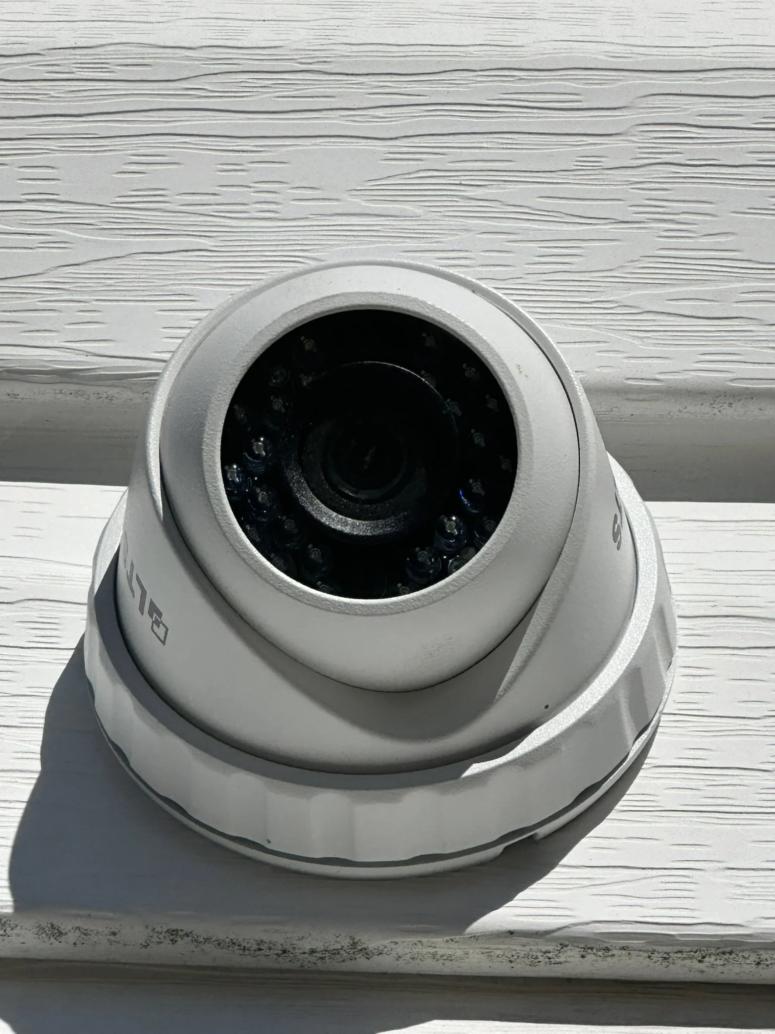 Close-up of a white security camera mounted on a white wooden surface with visible grain pattern.