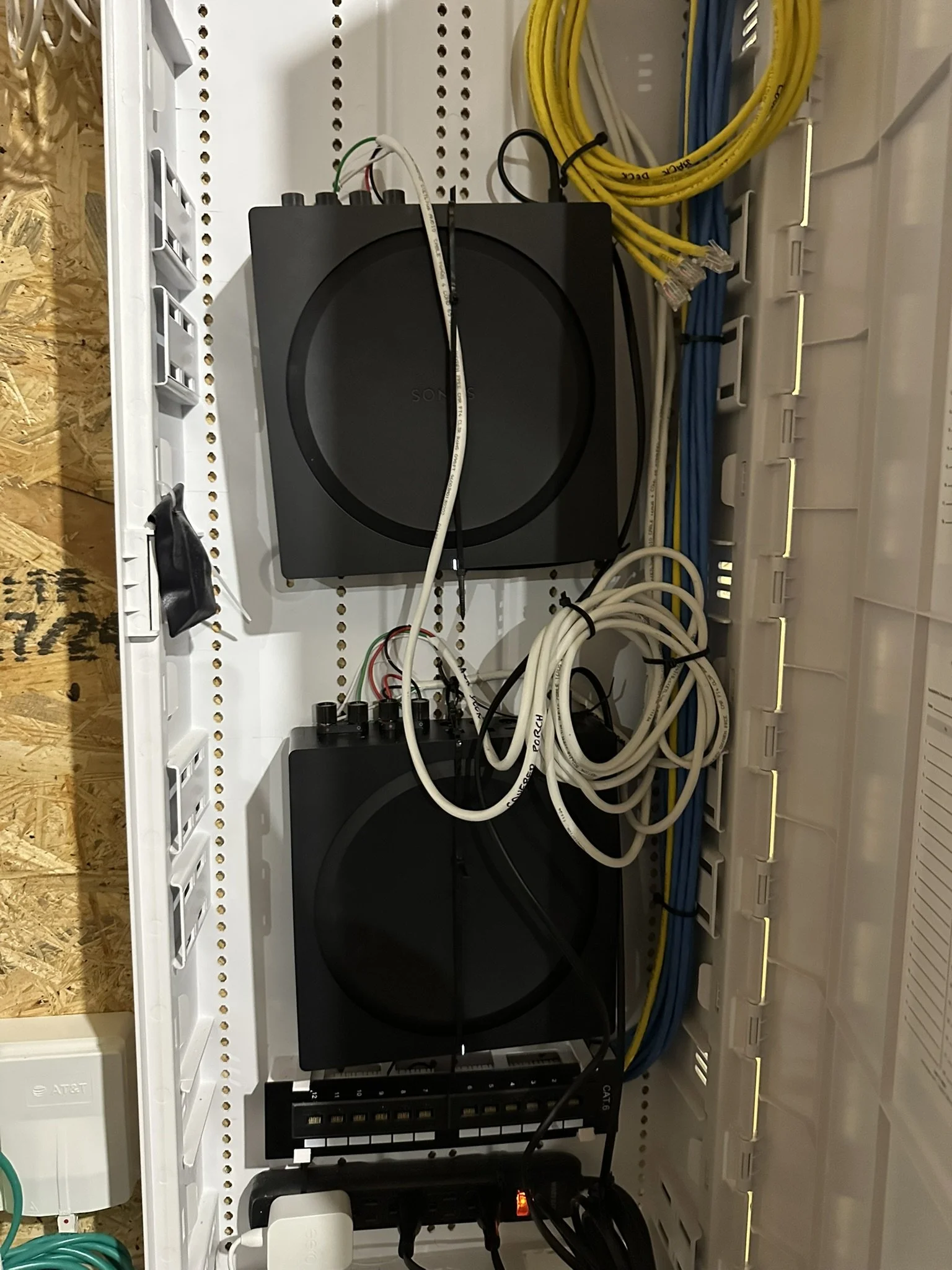An electrical panel containing two black Sonos subwoofers connected with wires, alongside bundled yellow and blue cables.