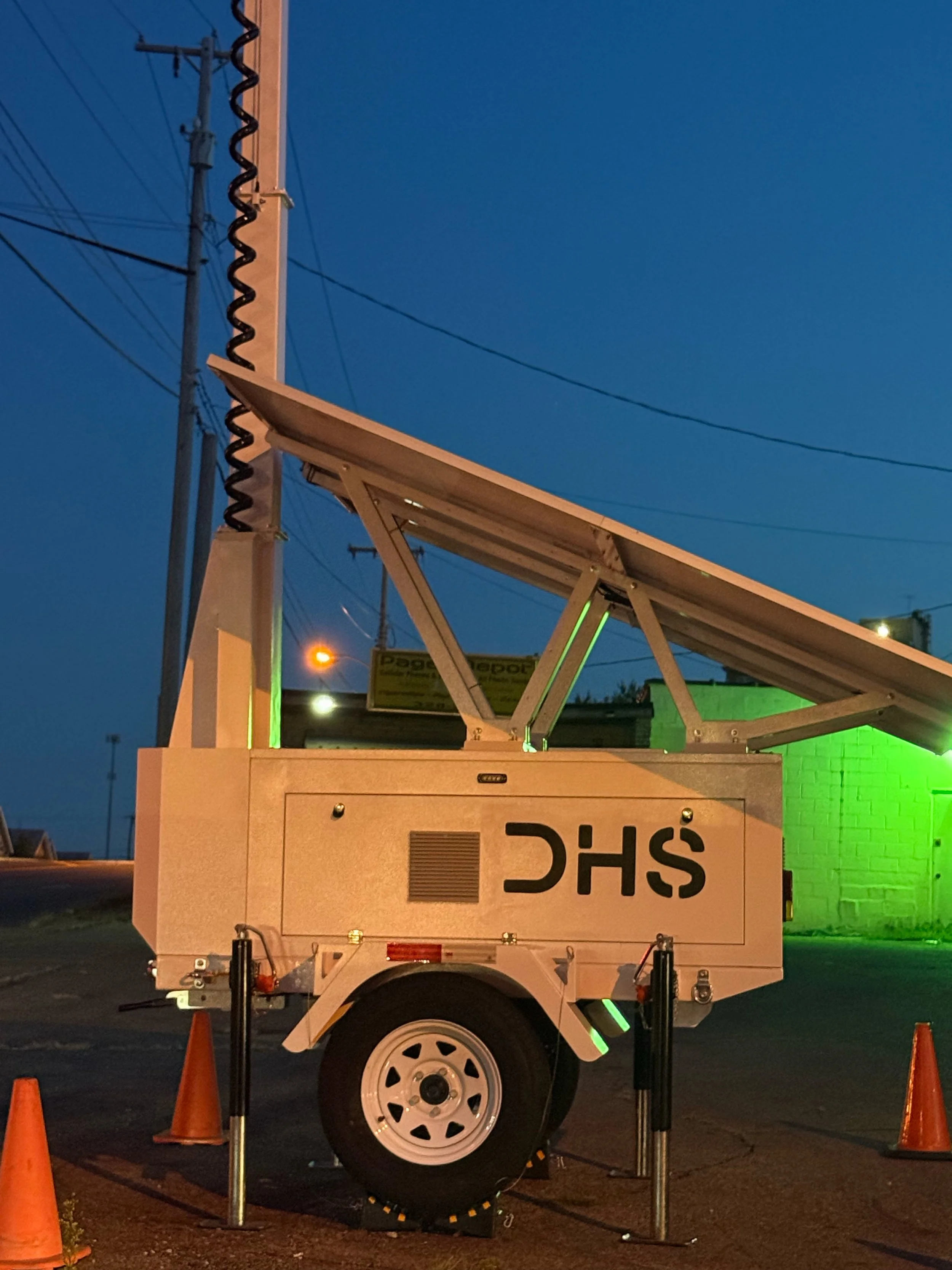 A utility truck with equipment set up for maintenance work, parked in a lot with orange traffic cones, under a dark blue sky.