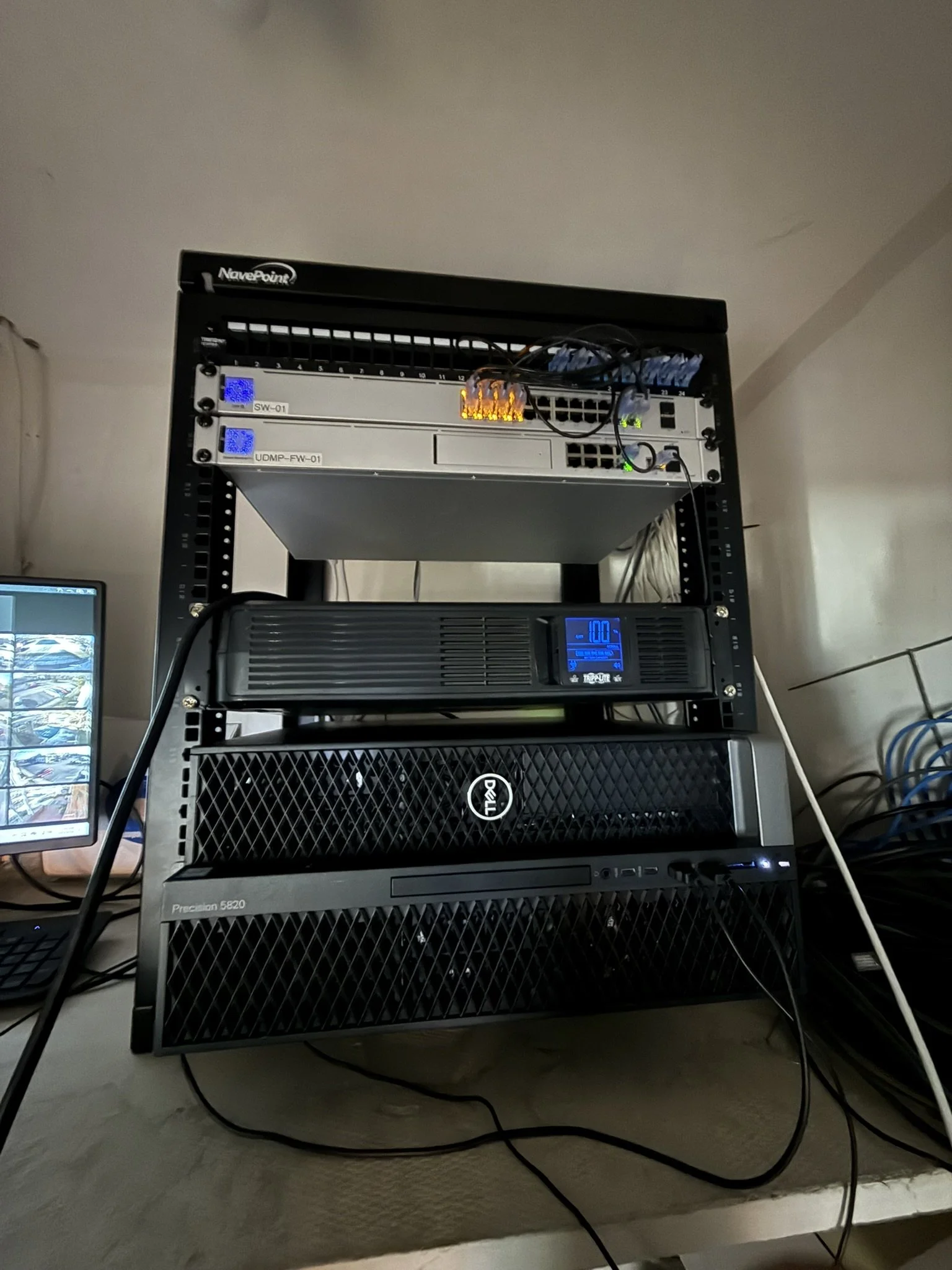 Server rack with networking equipment, switches, and a UPS, placed on a light-colored wooden table.