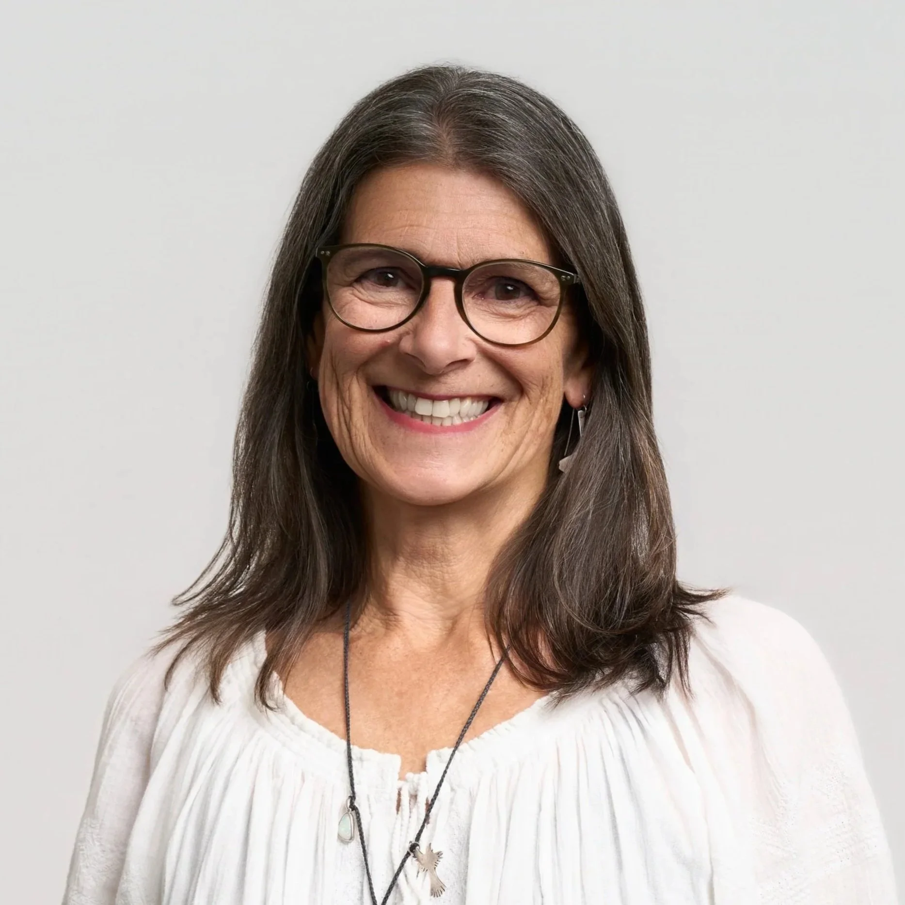 An older woman with gray hair wearing glasses and a black top, smiling at the camera.
