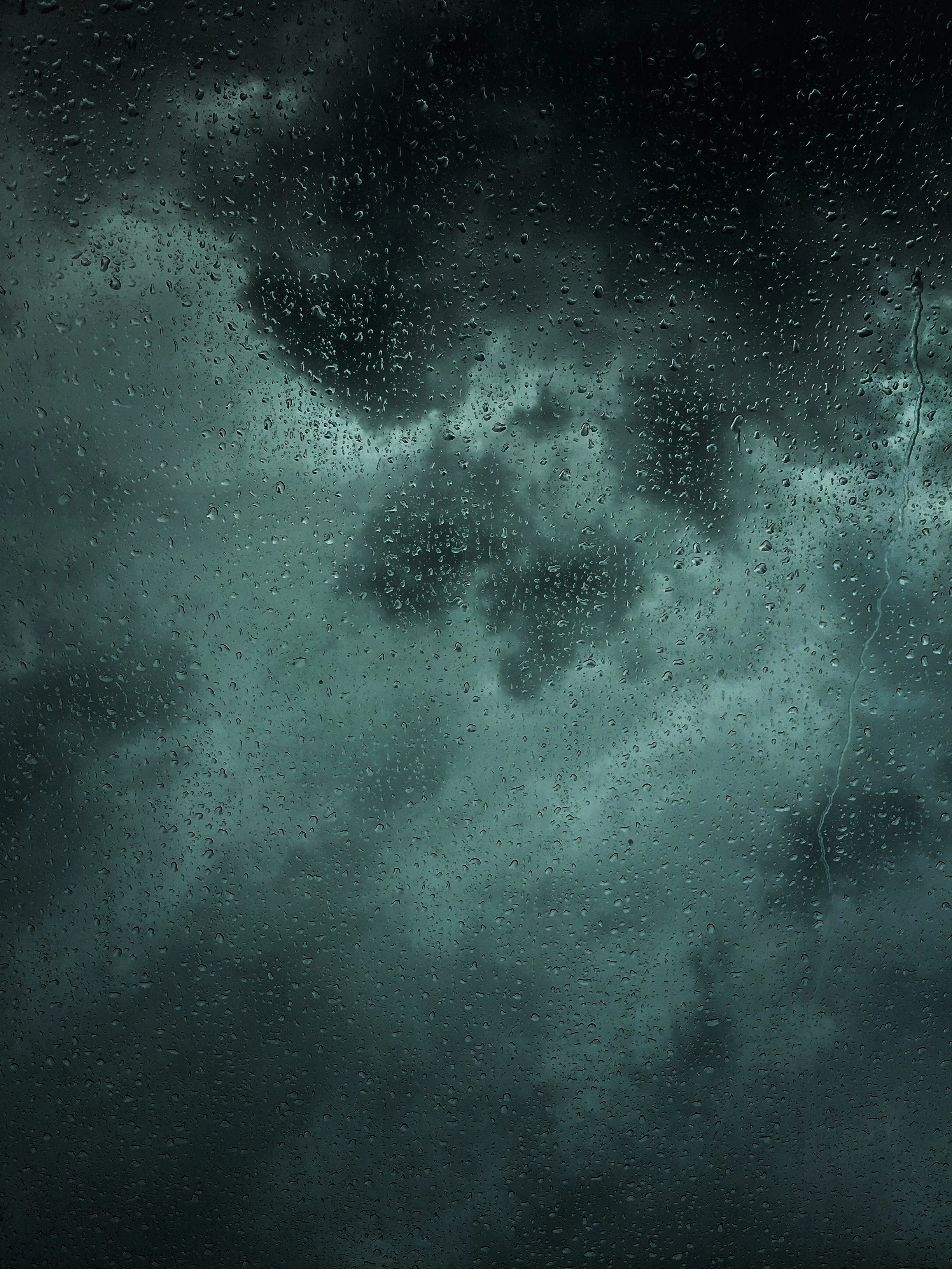 Dark, stormy sky with large clouds, viewed through a rain-speckled window, indicating heavy rain and threatening weather.