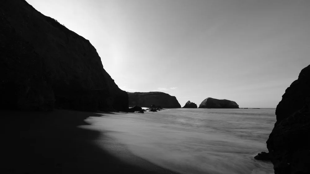 Black and white seascape framed by dark coastal cliffs