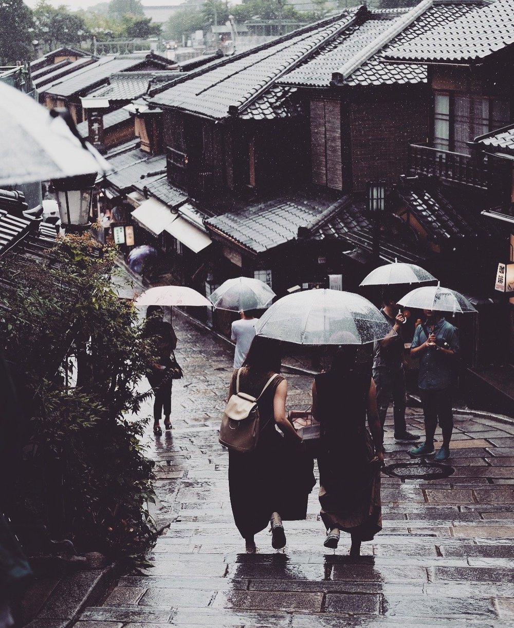 Two people with umbrellas walking along a traditional street in the rain