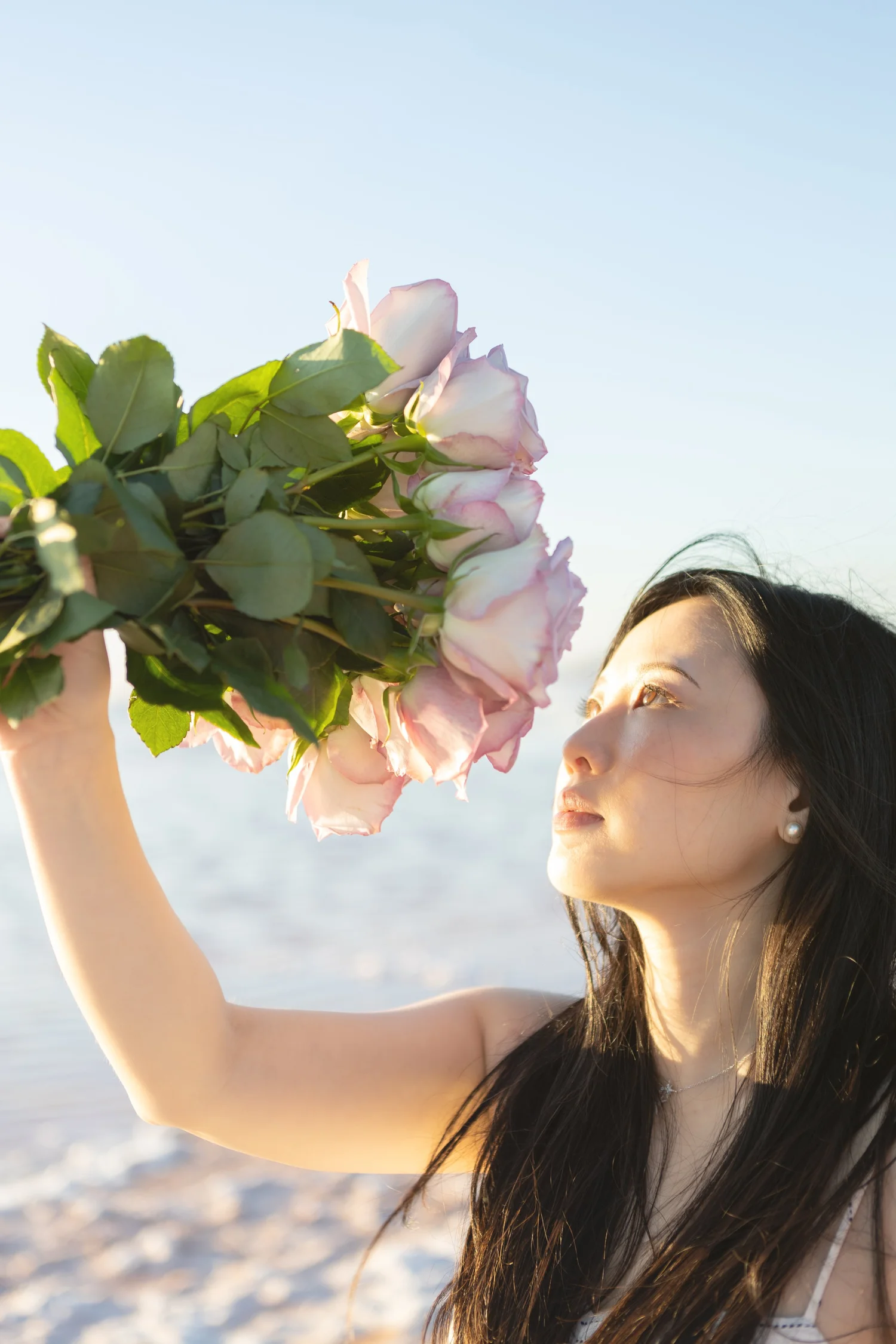 Sunlit portrait of a woman holding pale roses against a clear blue sky